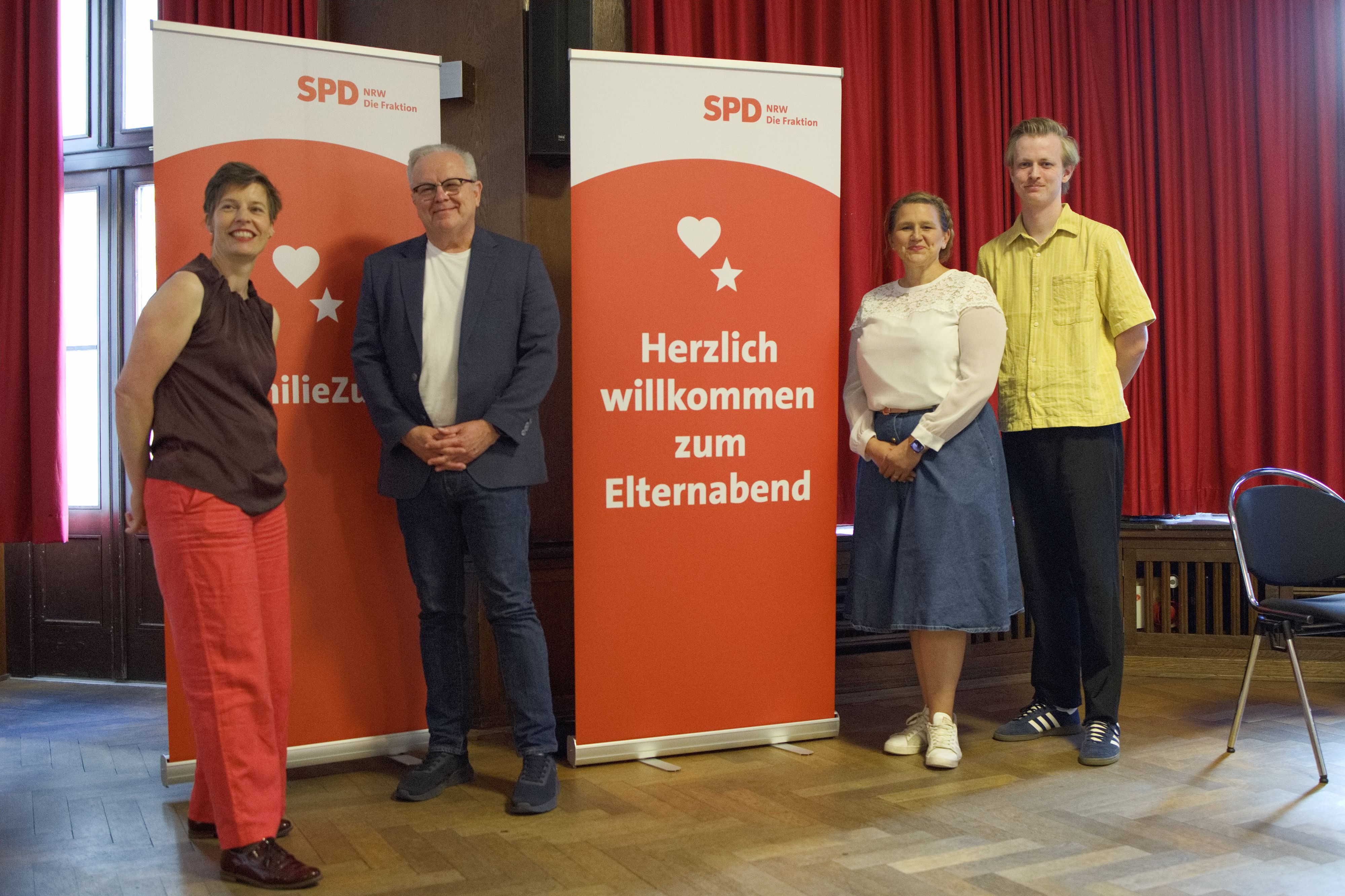 Die Obengenannten stehen neben zwei Plakaten, die auf die Veranstaltung hinweisen.