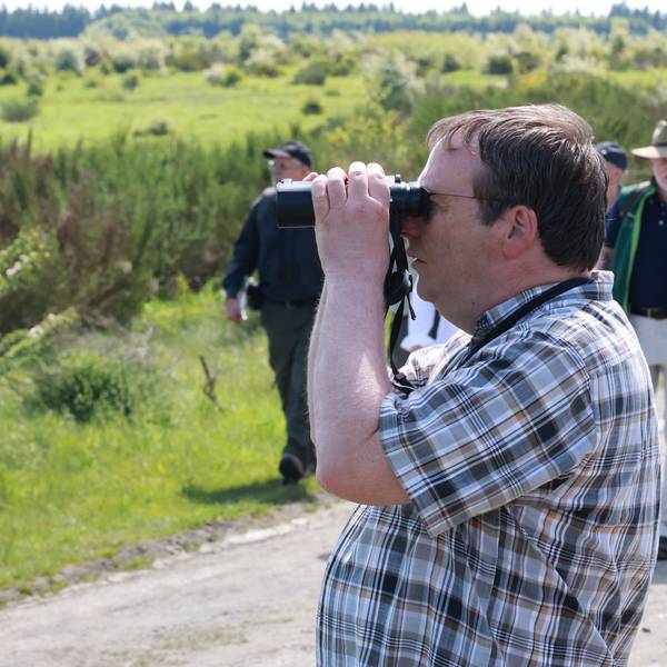 Der Minister blickt durch ein Fernglas auf die Vegetationn neben dem Weg. Hinter ihm weitere Mitwanderer.