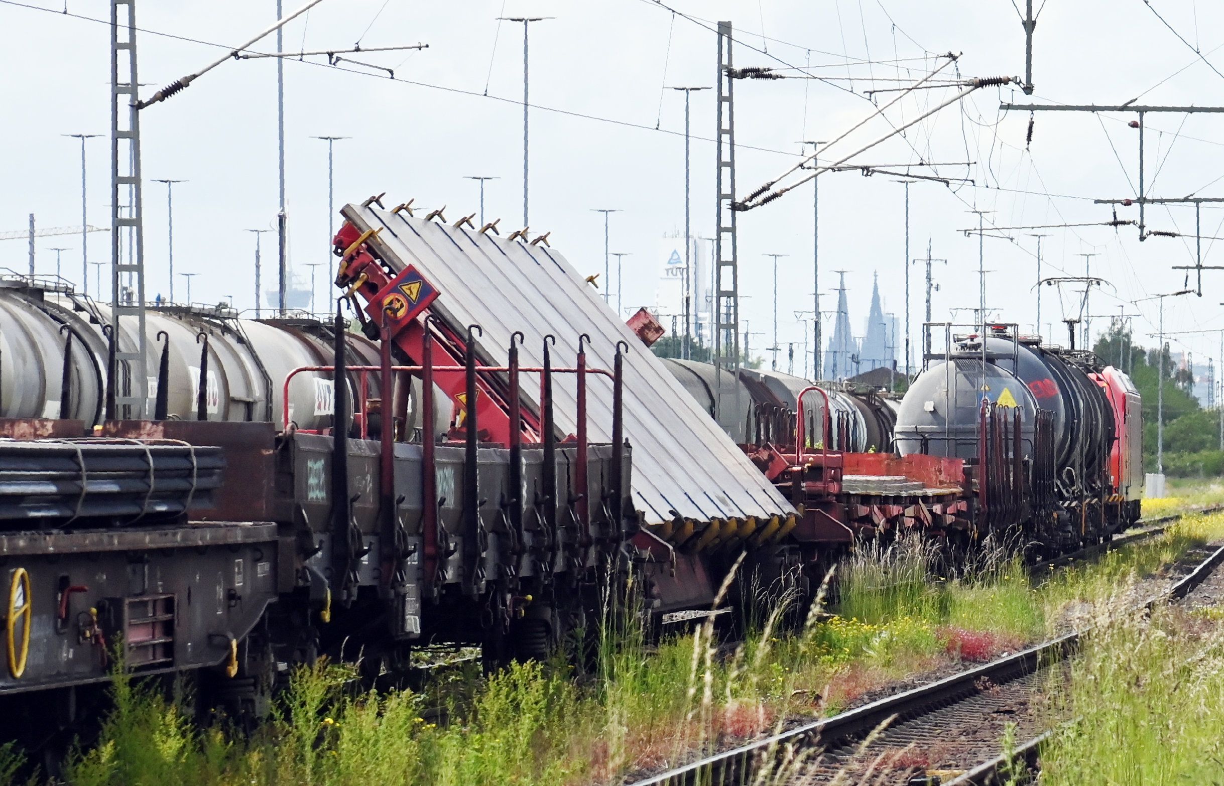 Mehrere Güterwagen in einer Reihung, einer ist mit einer sehr großen Stahlplatte beladen, die schräg auf dem Waggon befestigt ist.