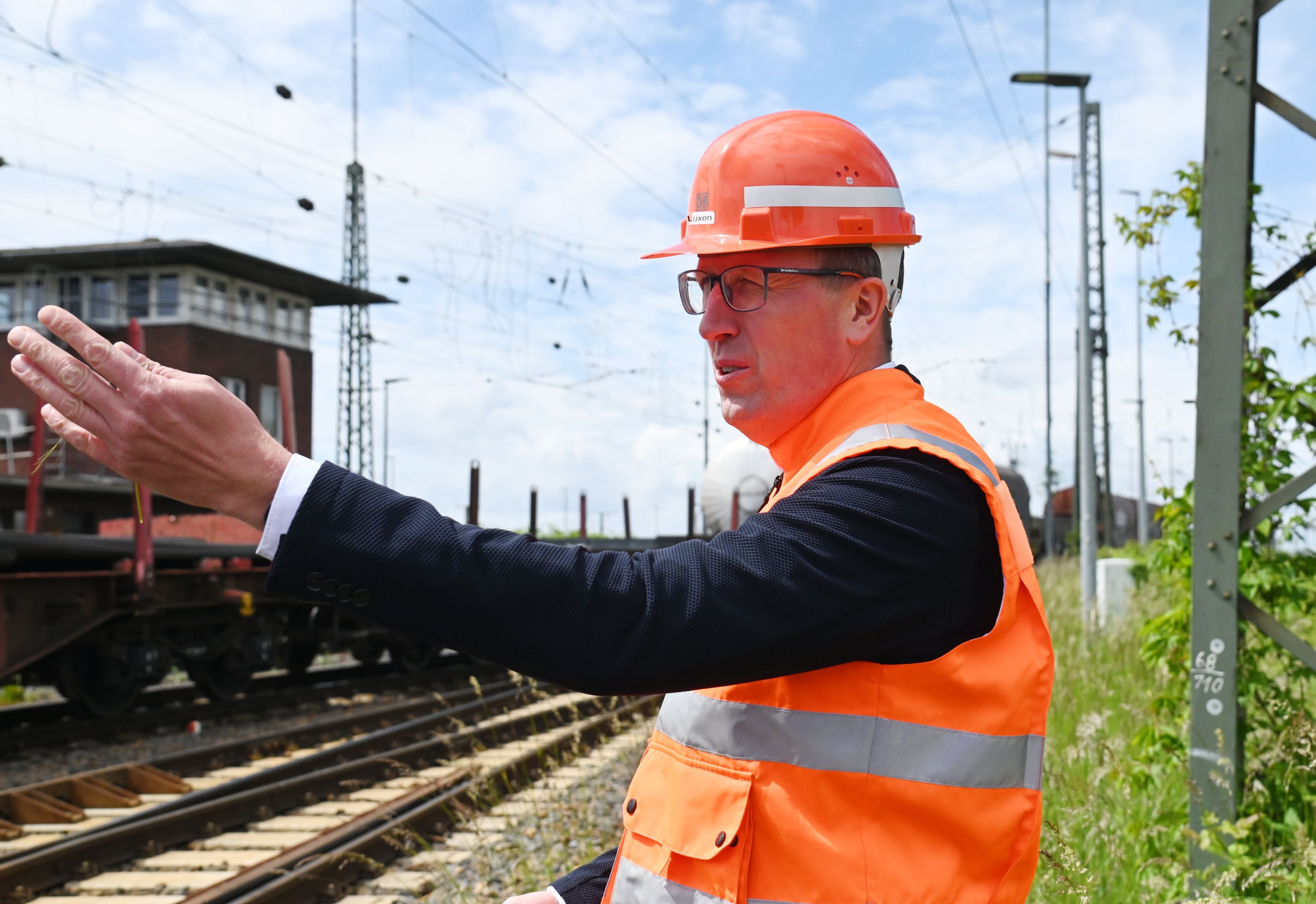 Herr Luxen steht an den Gleisen in orangefarbener Weste und mit Schutzhelm und erklärt etwas.