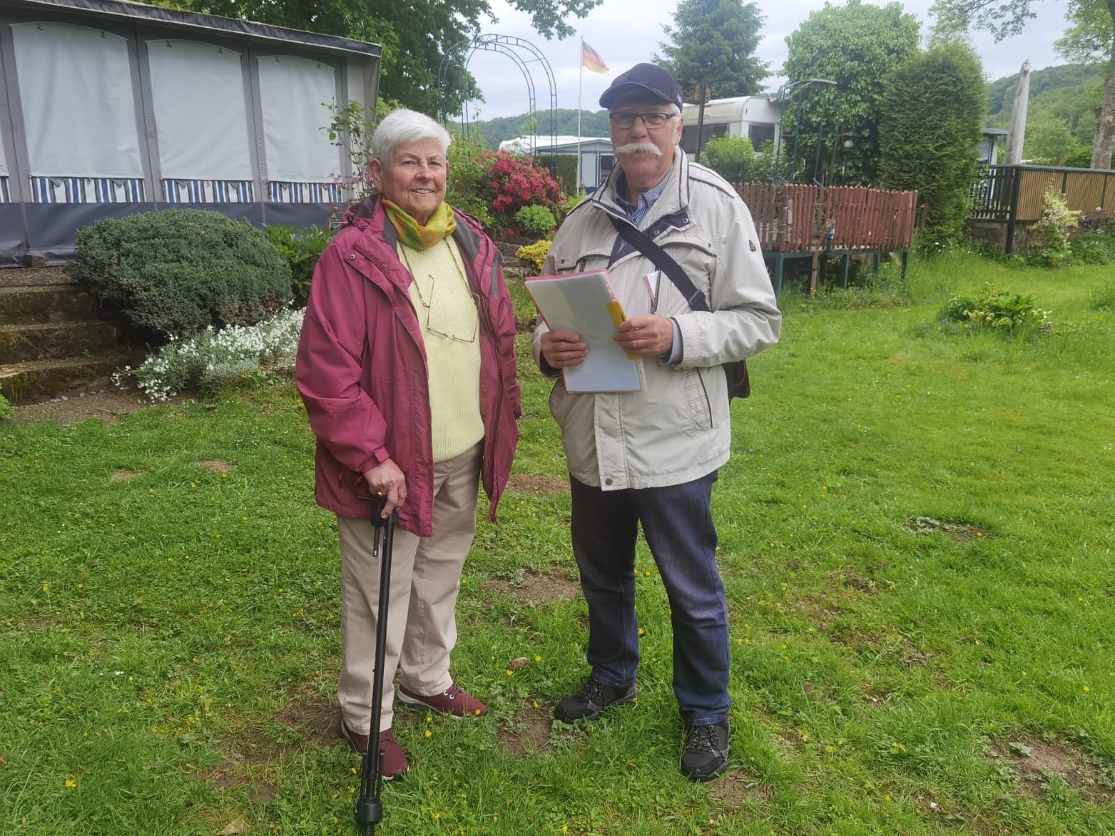 Eine Frau und ein Mann stehen nebeneinander und lächeln. Der Mann hält einige Bögen Papier in der Hand.