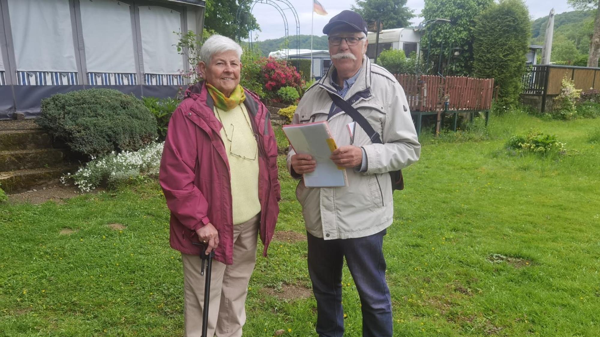 Eine Frau und ein Mann stehen nebeneinander und lächeln. Der Mann hält einige Bögen Papier in der Hand.