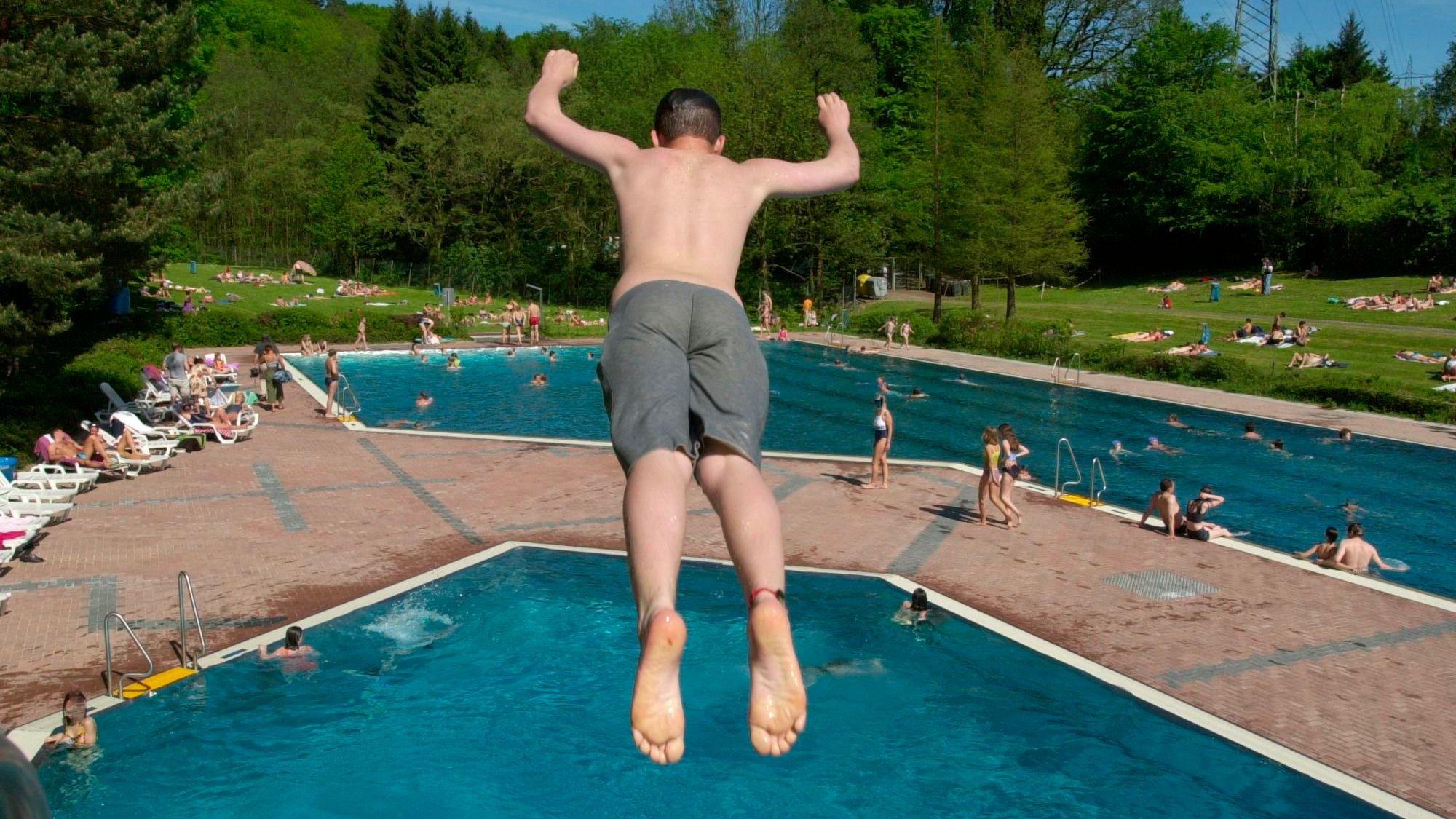 Ein junger Mann springt von einem Springturm in das Wasserbecken im Freibad Milchborntal.