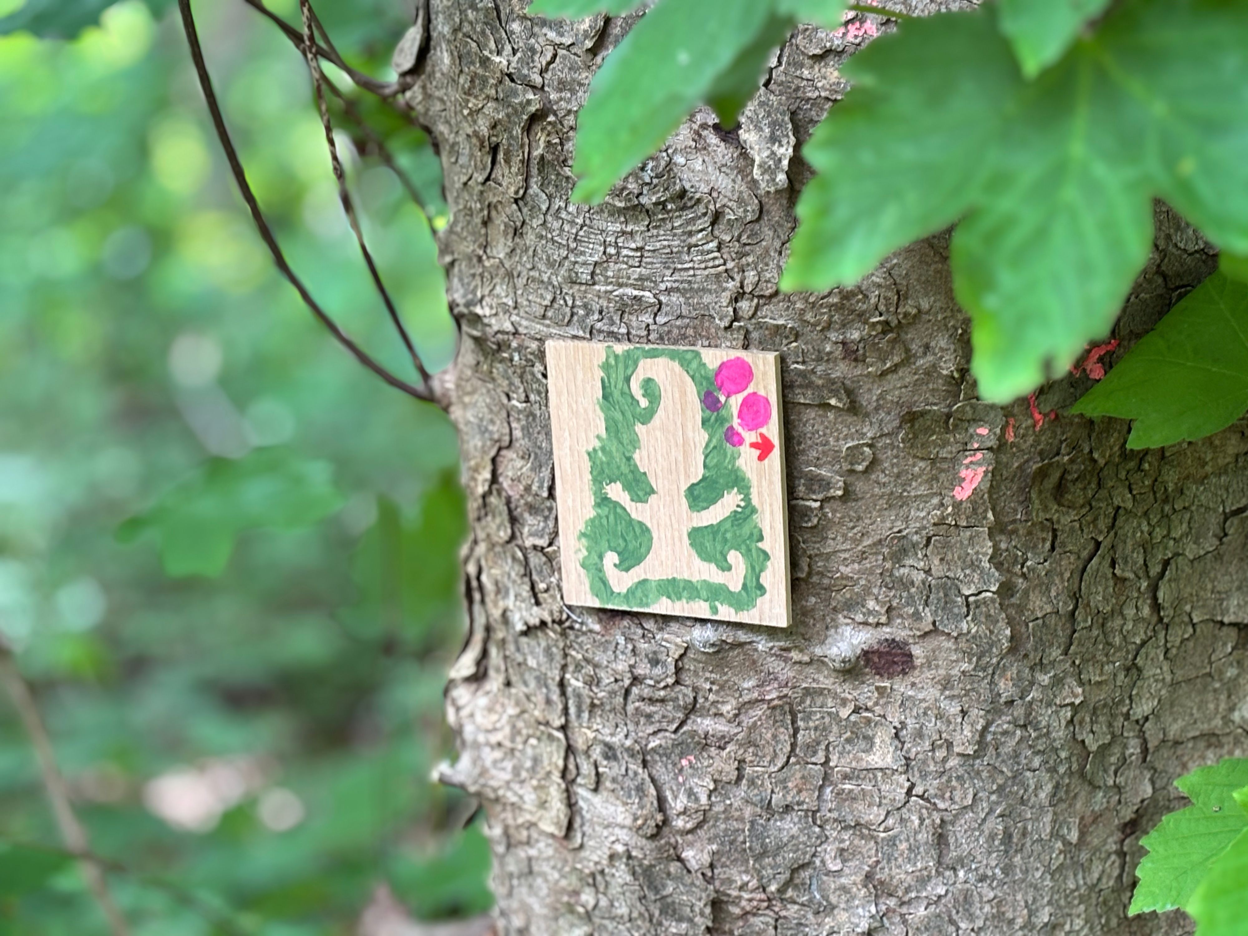 Auf einem Holzschild, das an einem Baum befestigt wurde, sind die Umrisse eines Wichtels und ein Pfeil aufgemalt.