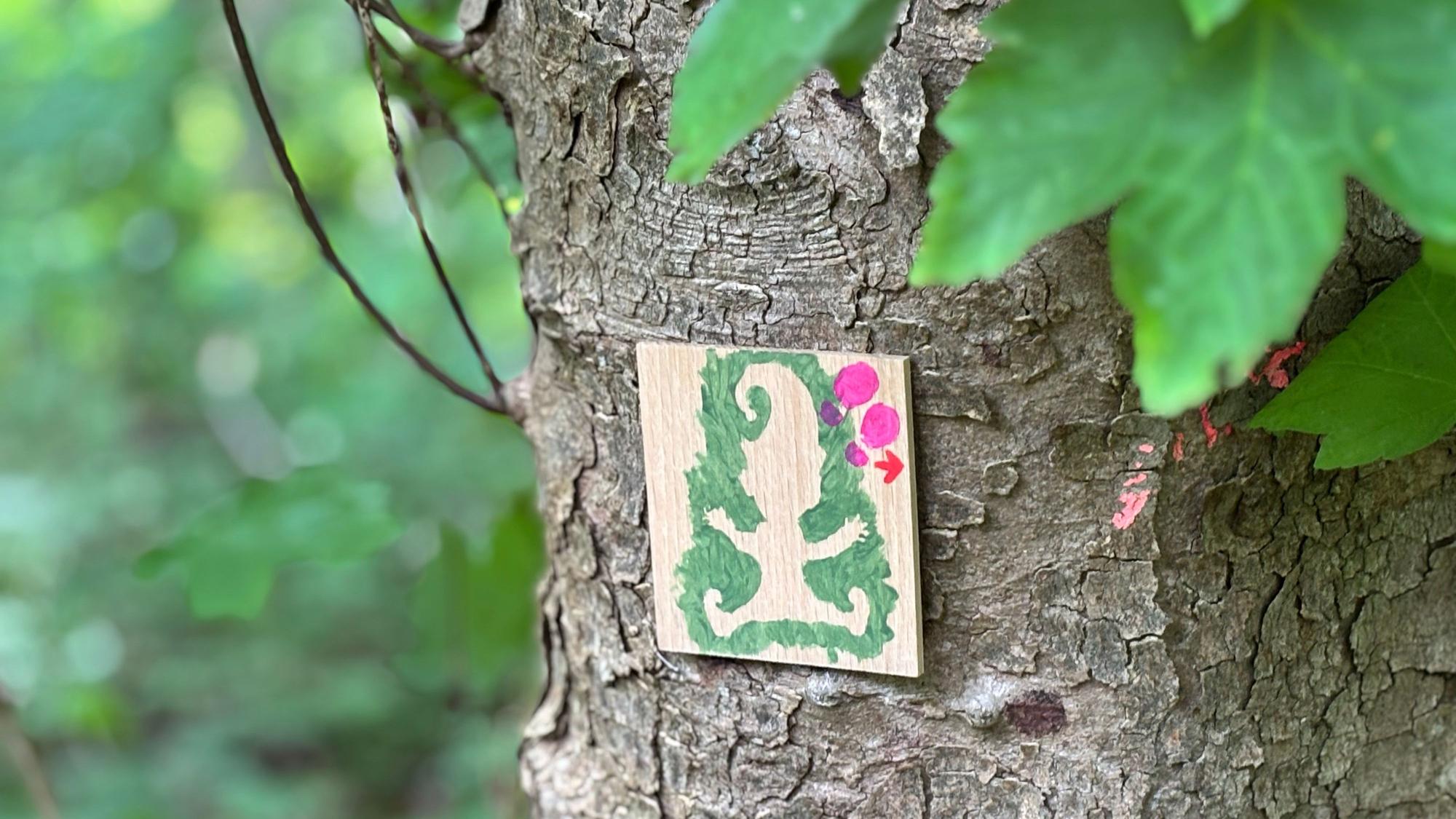 Auf einem Holzschild, das an einem Baum befestigt wurde, sind die Umrisse eines Wichtels und ein Pfeil aufgemalt.