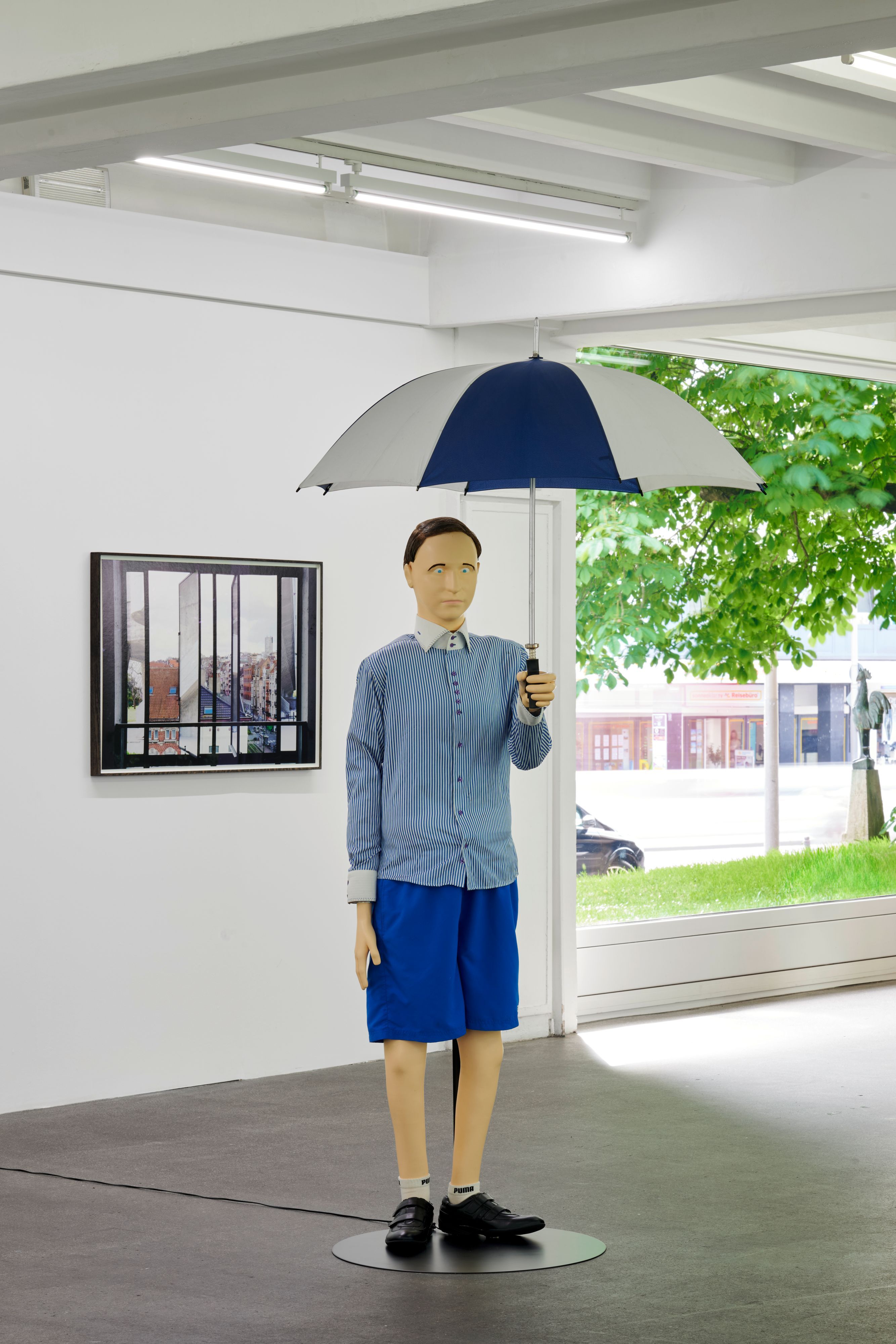 Eine lebensgroße Puppe hält einen Regenschirm in der Hand.