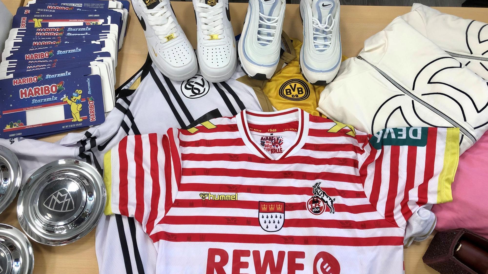 Gefälschte Fußballtrikots, Sneaker, Kleidungsstücke und andere Artikel liegen auf einem Tisch.