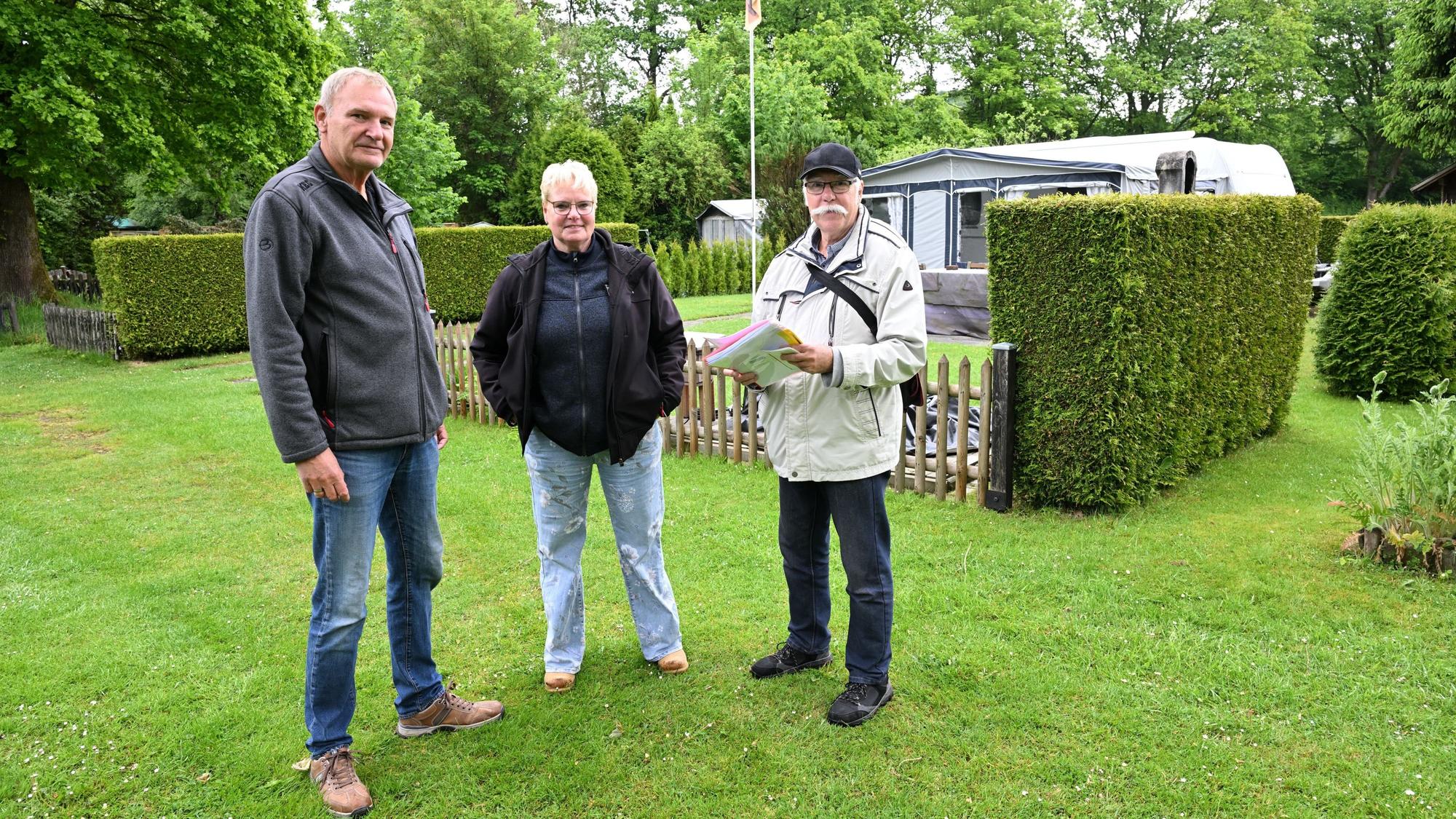 Zwei Männer und eine Frau stehen auf dem Rasen eines Campingplatzes.