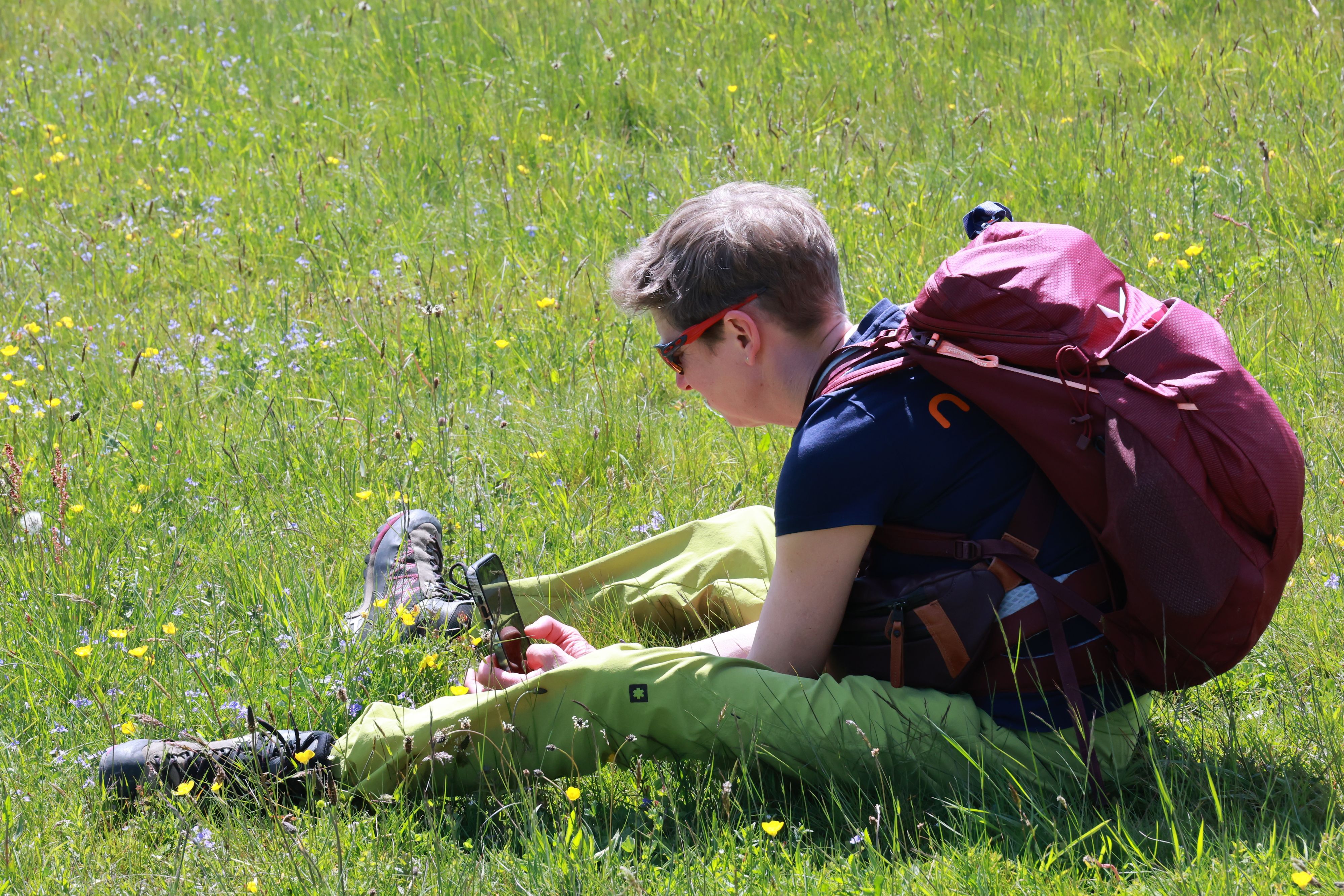 Ein Teilnehmerin sitzt auf der Wiese und fotografiert mit dem Handy eine Blume.