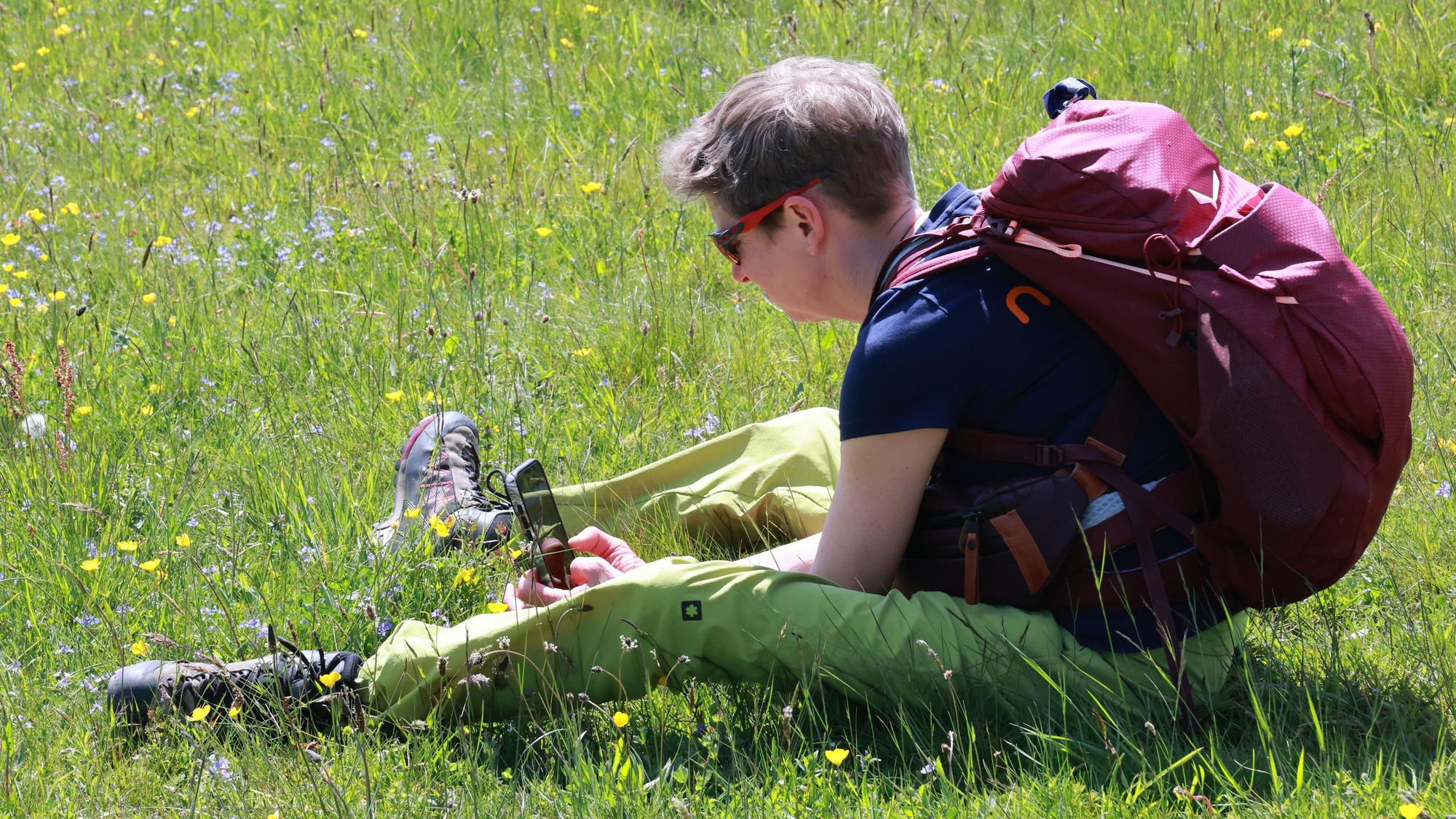 Ein Teilnehmerin sitzt auf der Wiese und fotografiert mit dem Handy eine Blume.