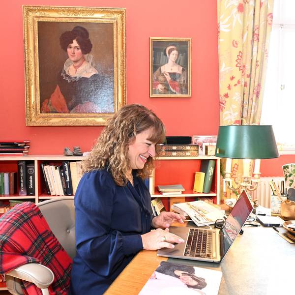 Eine Frau sitzt an einem Laptop in einem Arbeitszimmer mit historischen Ölporträts an den terrakottafarbenen Wänden.