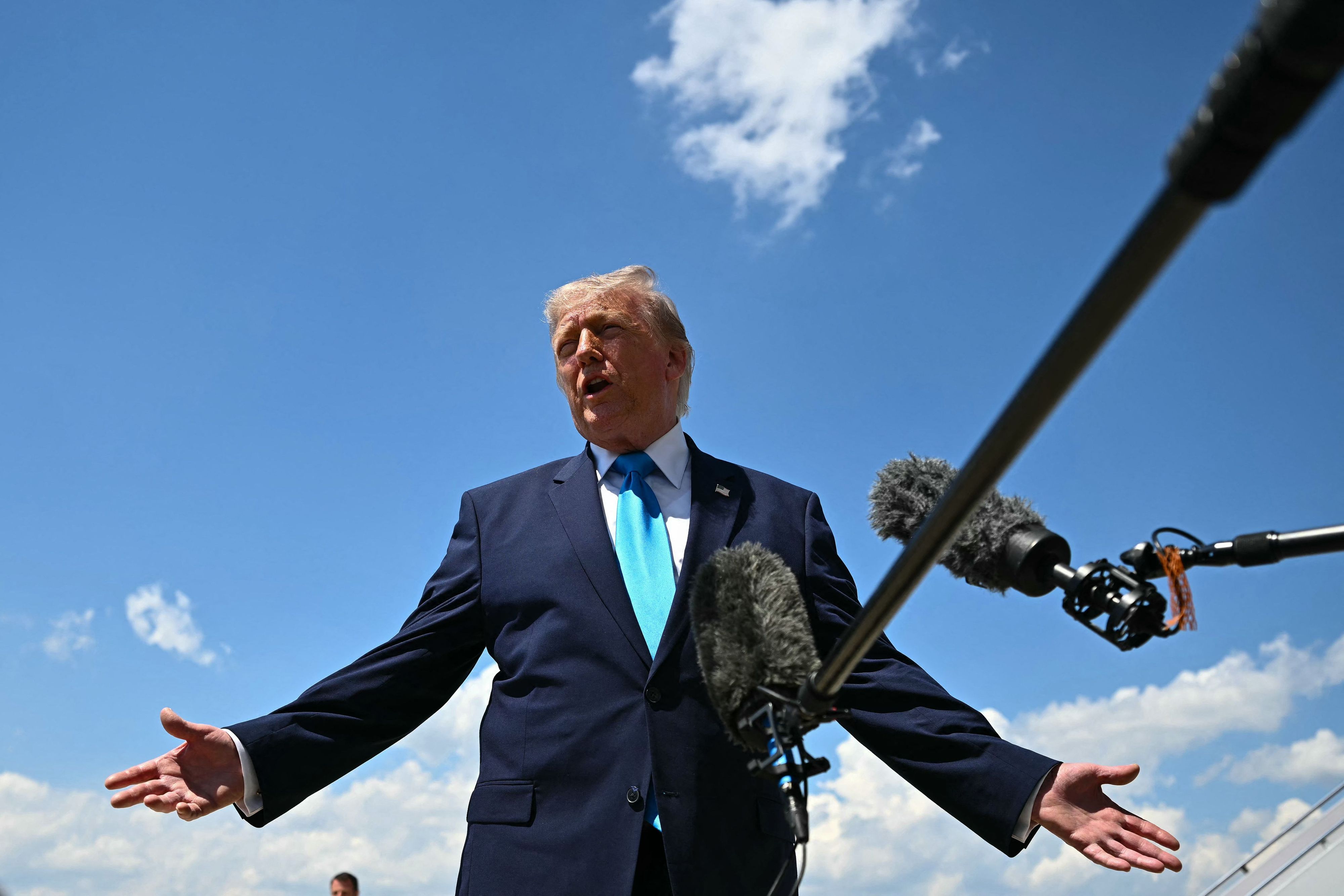 Donald Trump spricht vor blauem Himmel in ein Mikrofon.