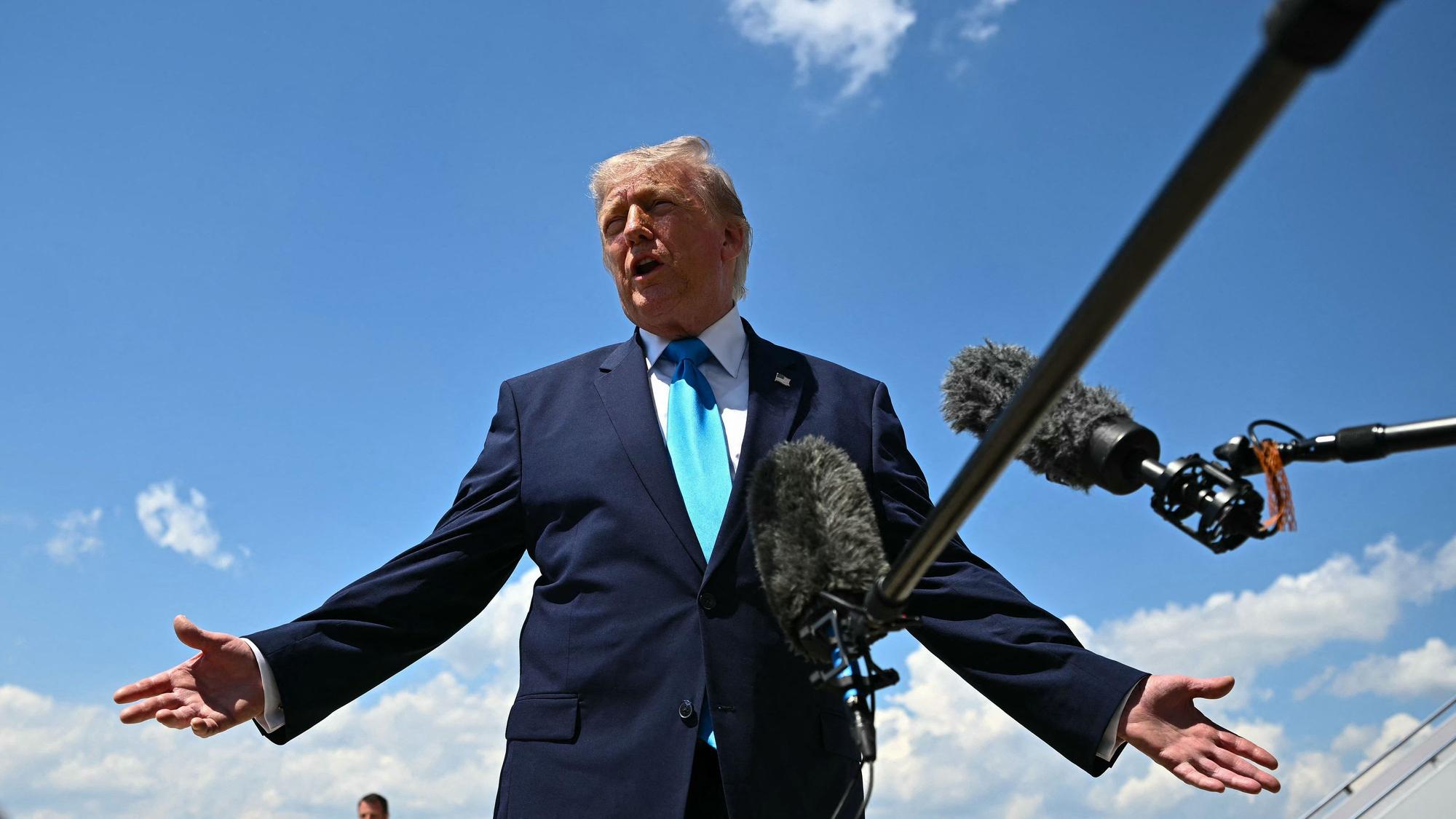 Donald Trump spricht vor blauem Himmel in ein Mikrofon.