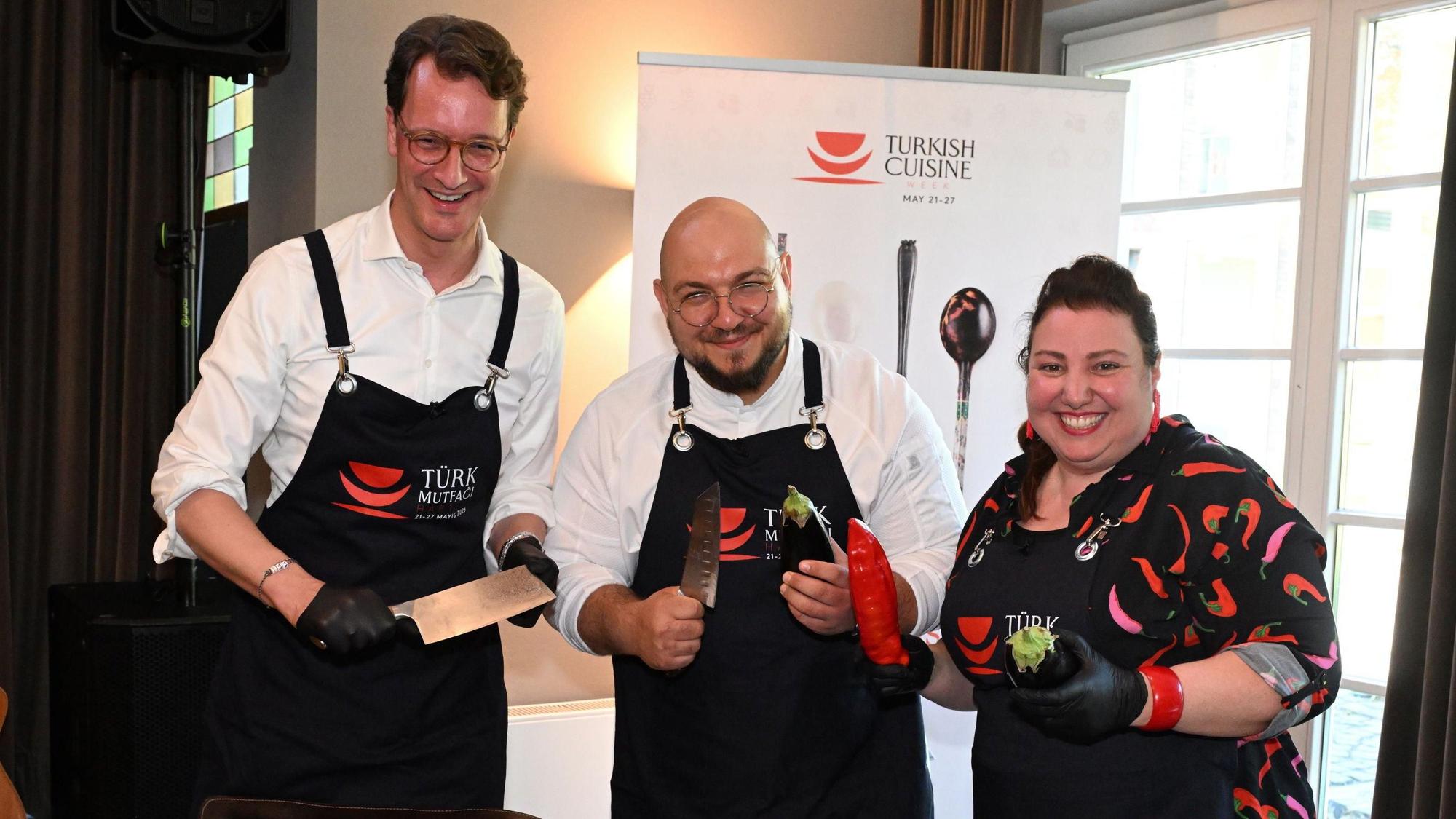 Ministerpräsident Hendrik Wüst, Influencer und Koch Ferdi Ünlü und Comedian Meltem Kaptan (v.l.) halten Gemüse und Messer in den Händen.