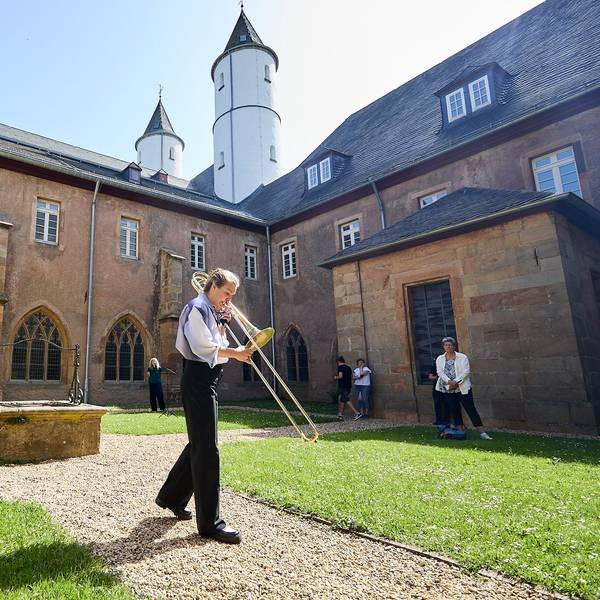 Maxine Troglauer steht bei Sonnenschein in einem Innenhof des Klosters in Steinfeld und spielt Posaune.