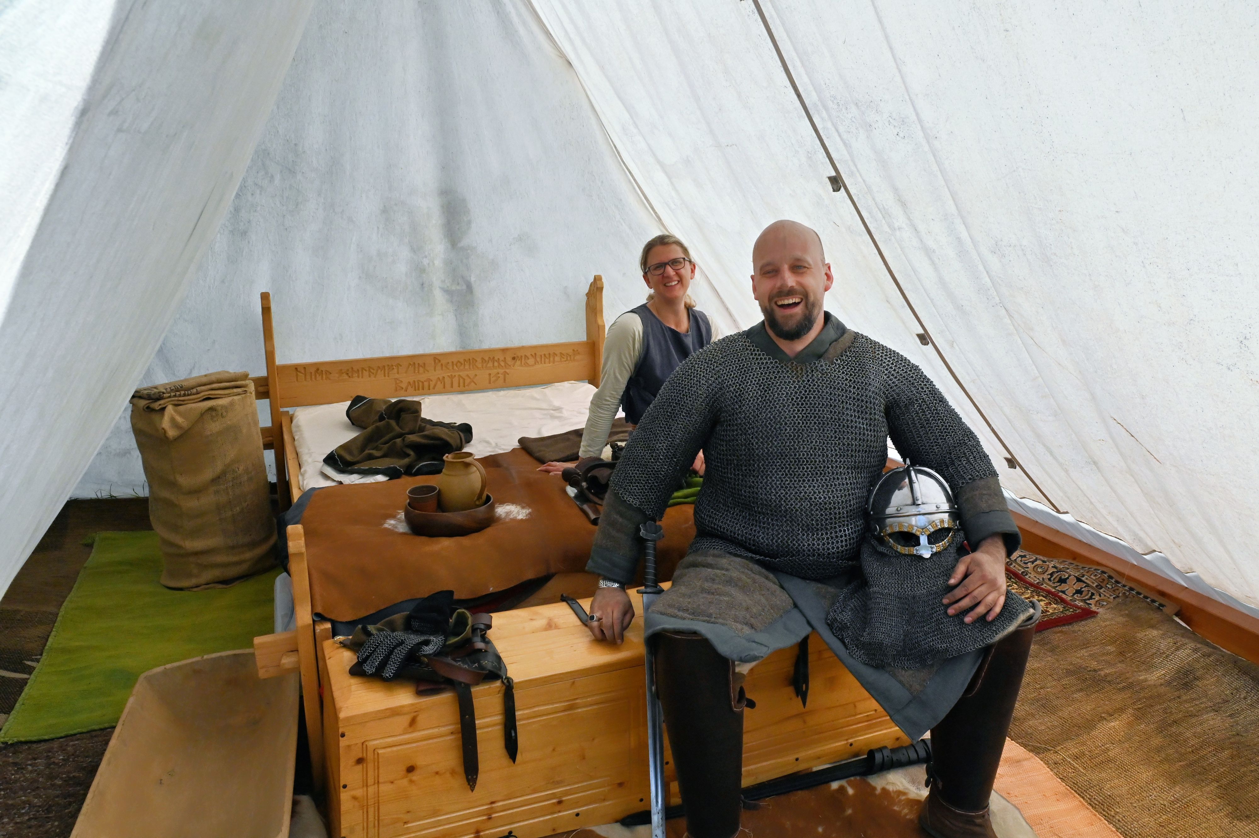 Ulrica und Torsten Radermacher sitzen an einem Holzbett in einem weißen Zelt.