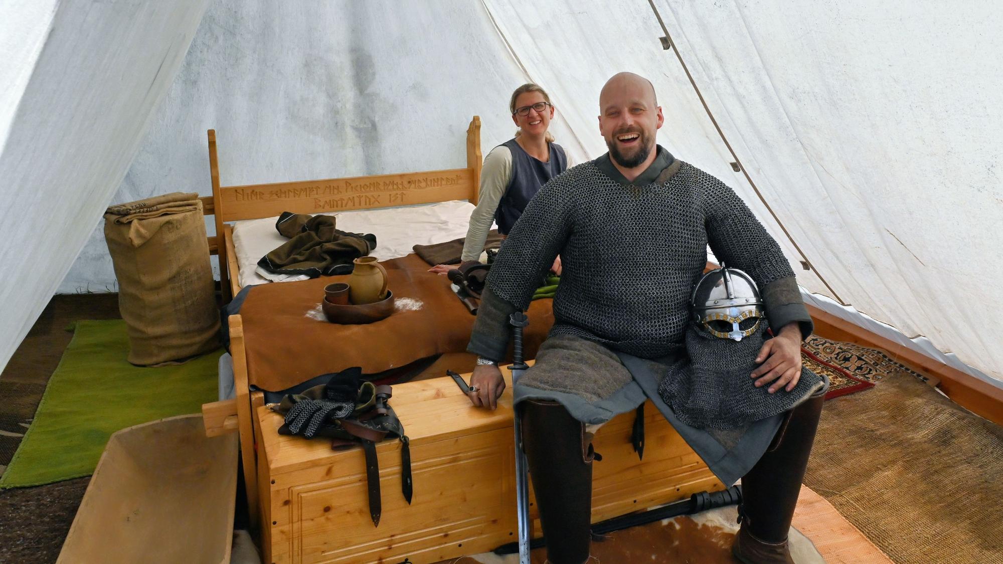 Ulrica und Torsten Radermacher sitzen an einem Holzbett in einem weißen Zelt.