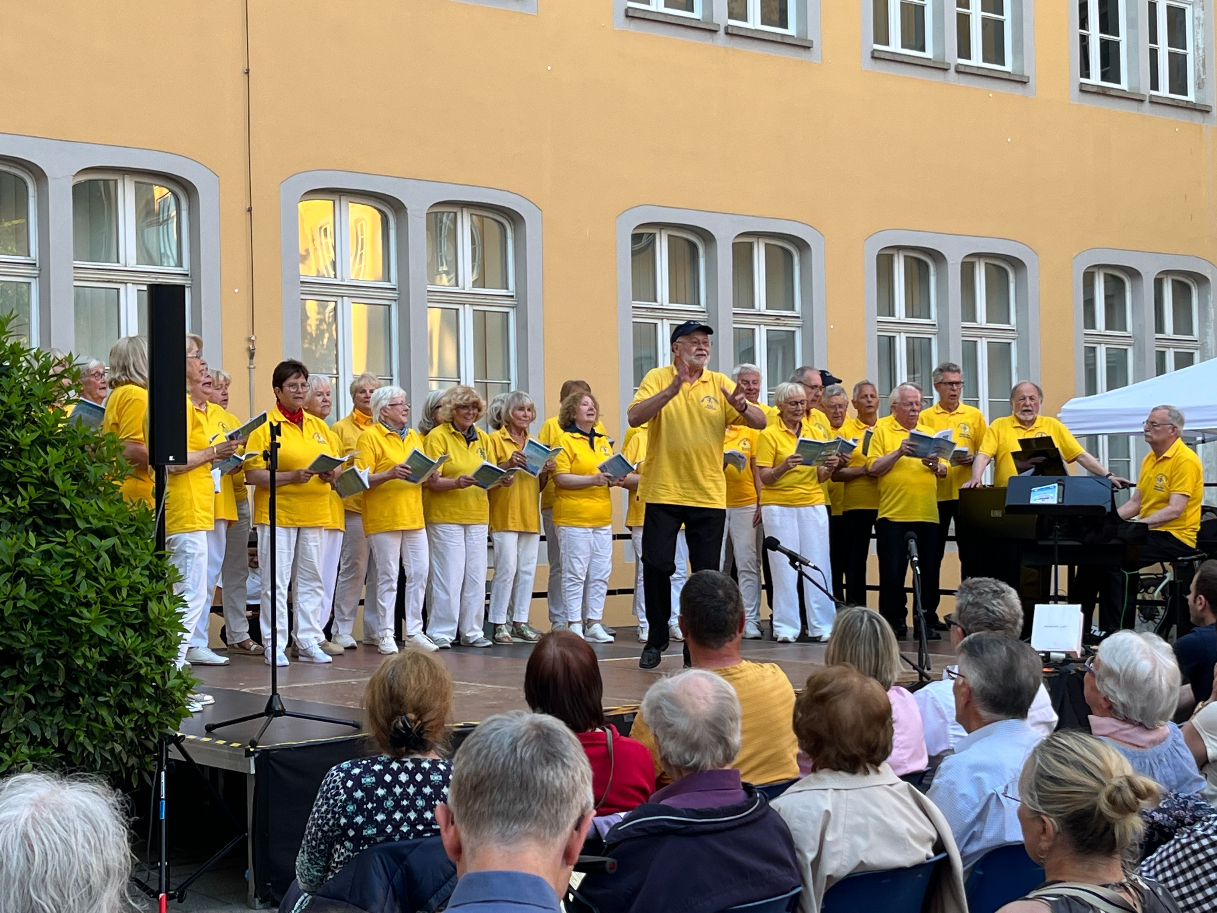 Zu sehen ist ein Chor beim Auftritt auf einer Bühne.