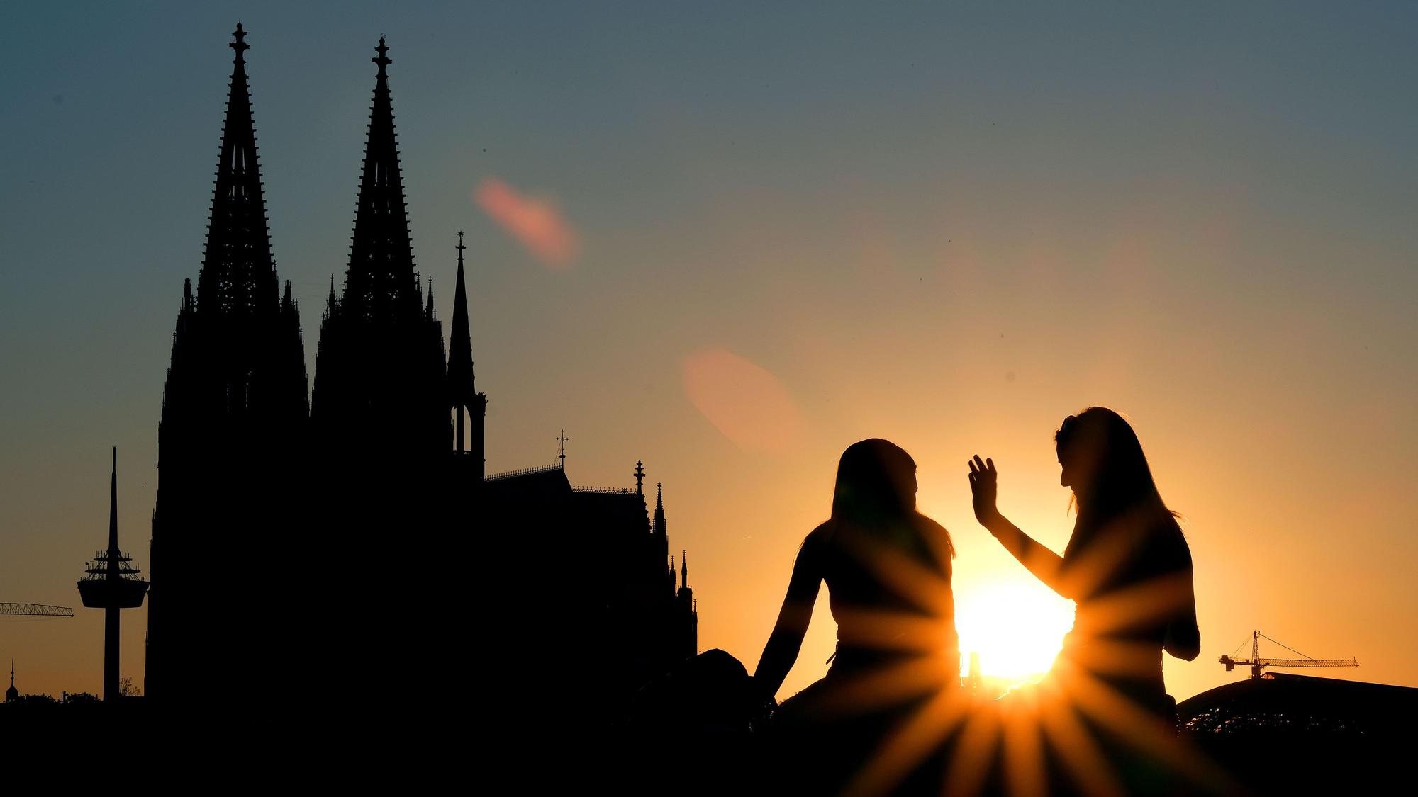 Zwei Frauen sitzen im Sonnenuntergang am Rheinboulevard vor dem Dom. (Archivbild)