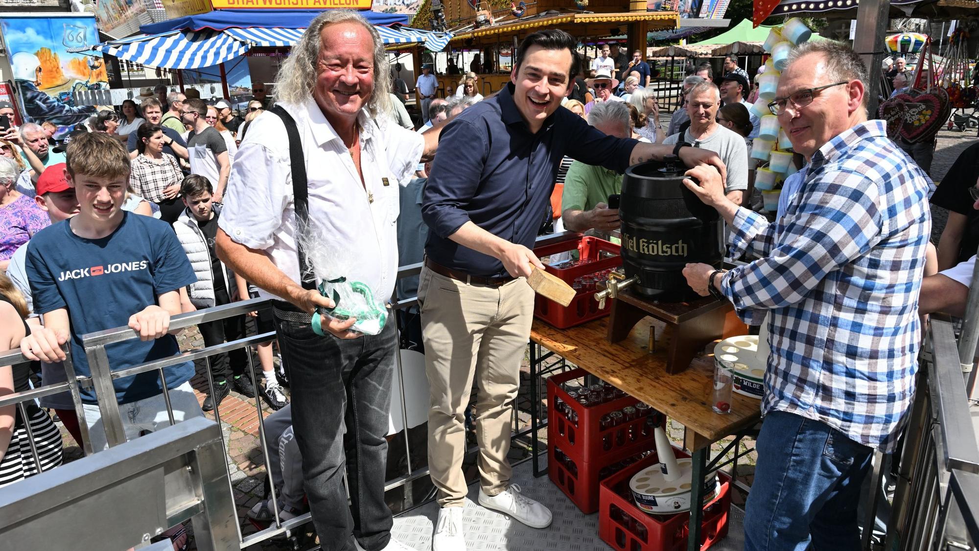 Drei Männer stehen vor einem Fass Kölsch und stechen es lächelnd an.