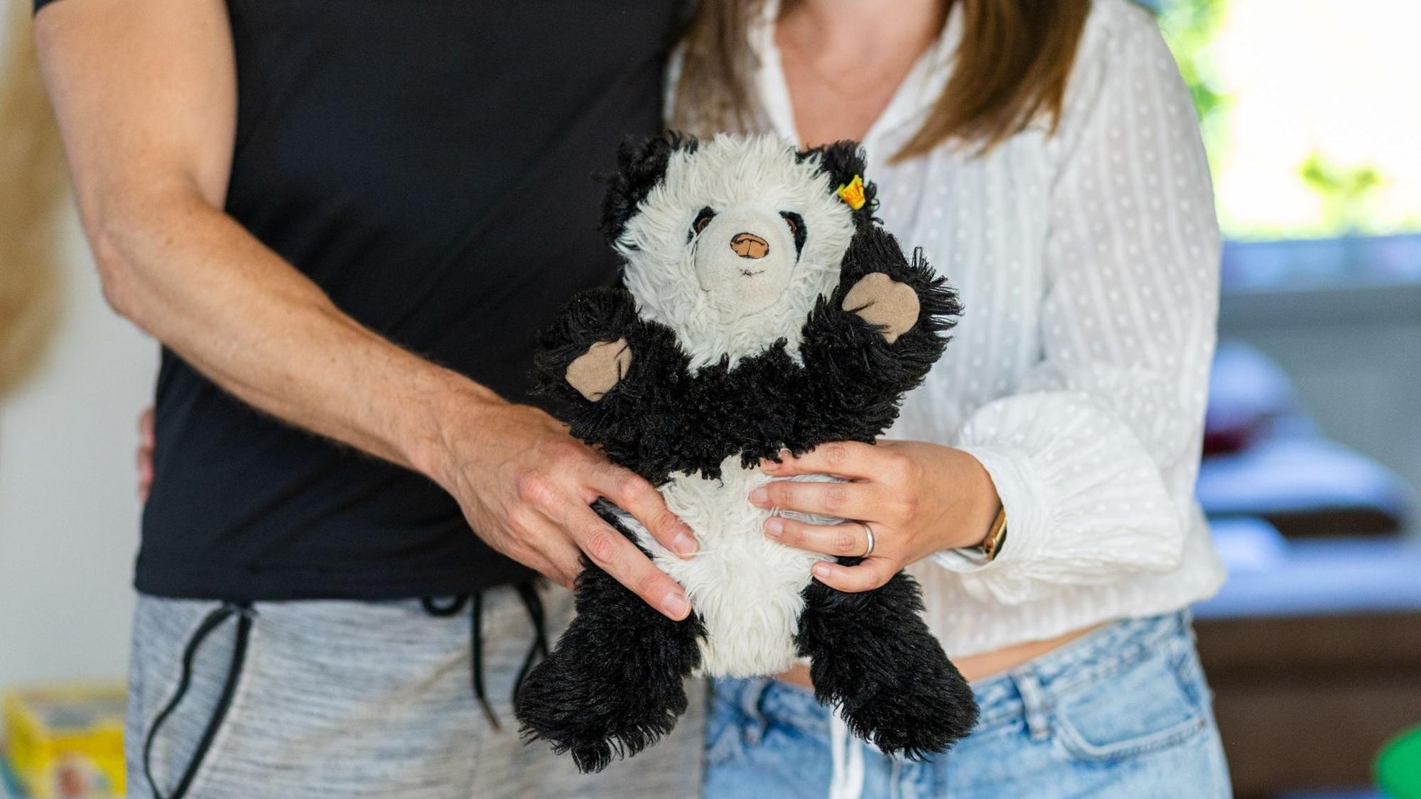 Ein Stoffpanda im Fokus, dahinter die Körper eines Mannes und einer Frau ohne Köpfe.