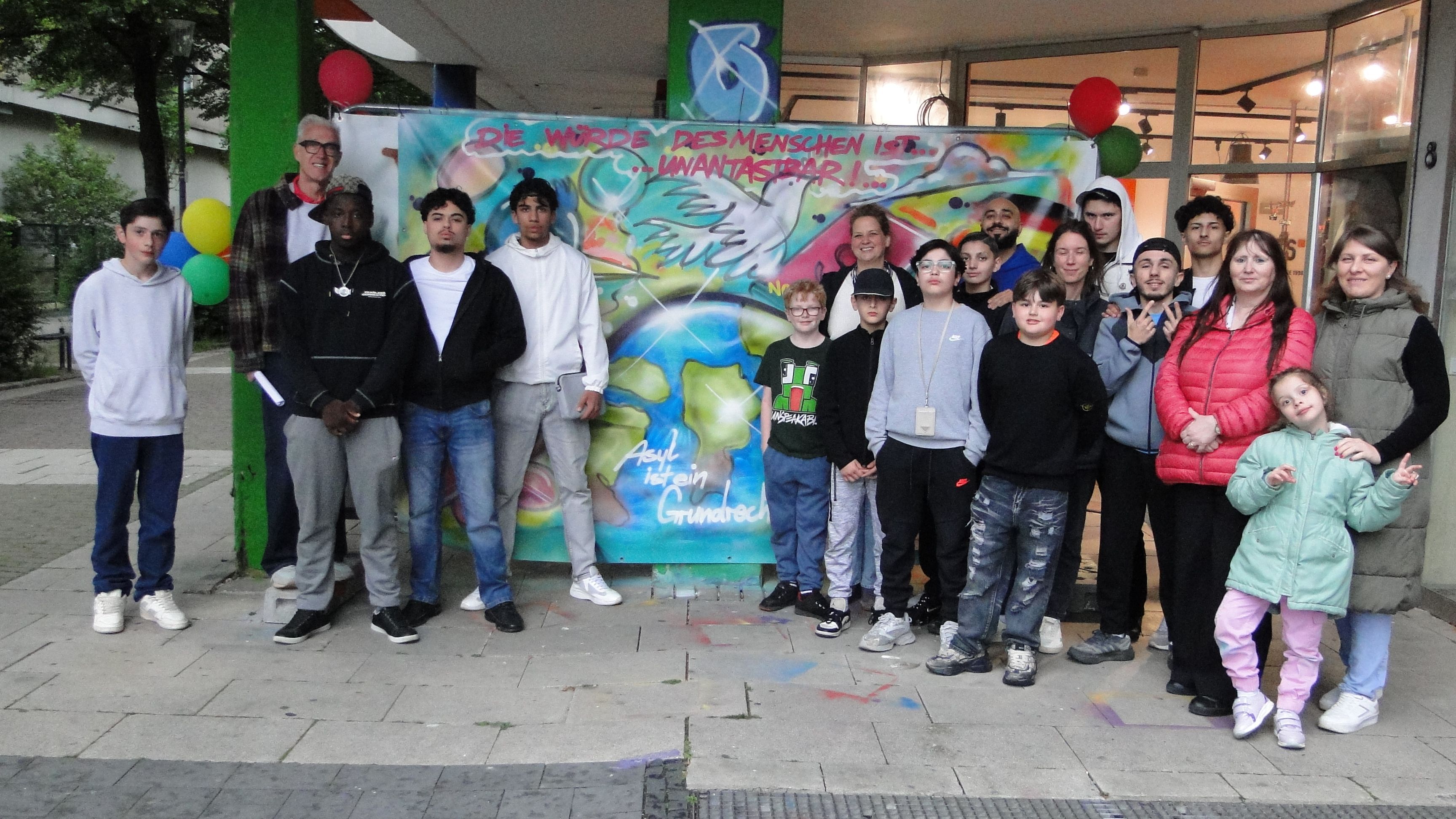 Ein großflächiges Graffiti und darum versammelte Menschen verschiedenen Alters