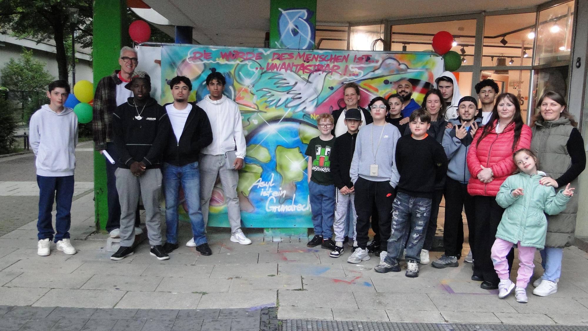 Ein großflächiges Graffiti und darum versammelte Menschen verschiedenen Alters