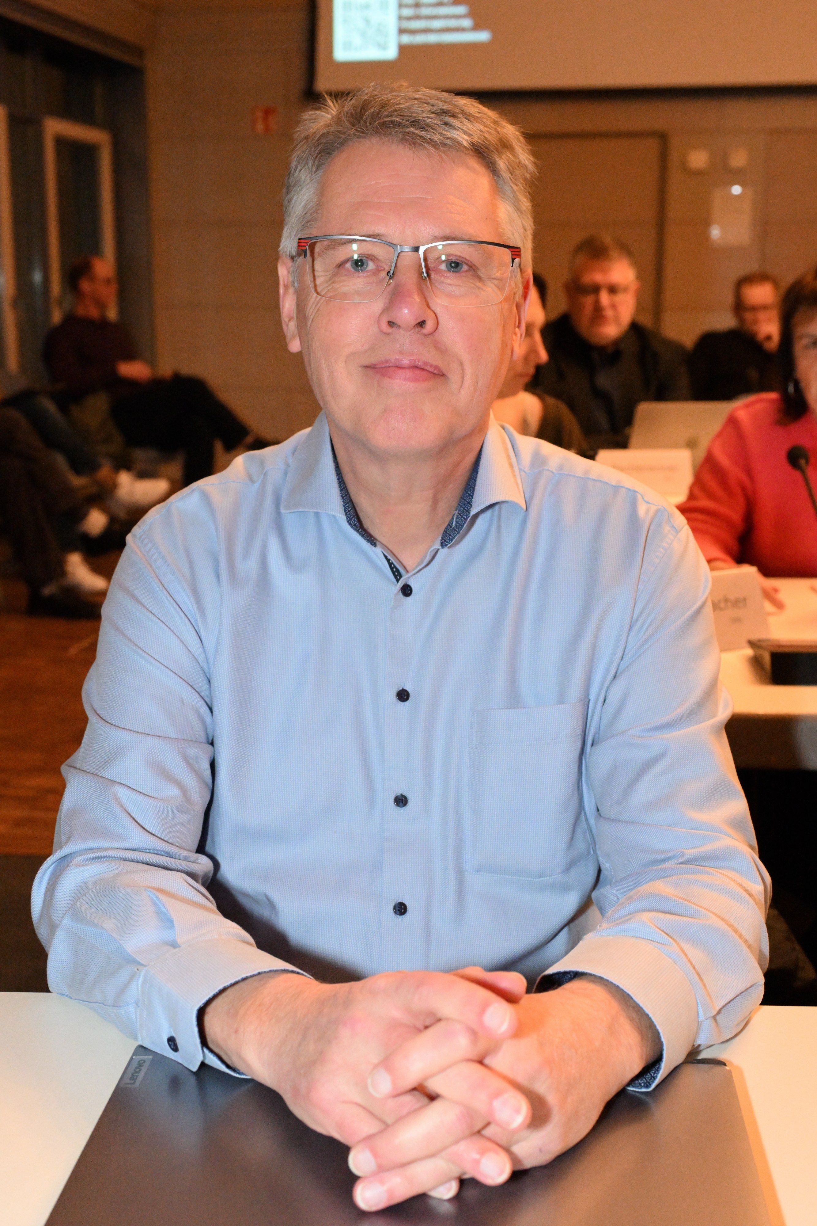 Ein Mann mit Brille sitzt in einem Ratssaal.