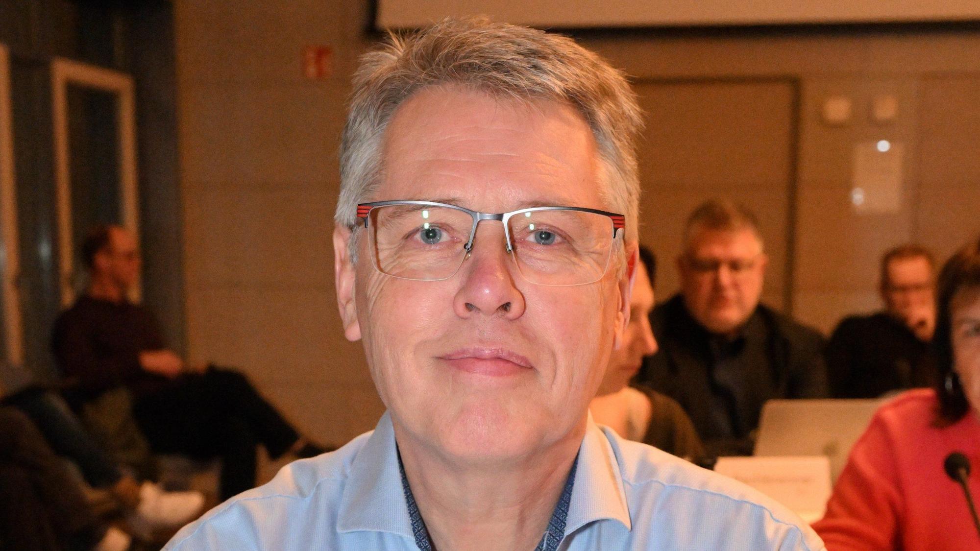 Ein Mann mit Brille sitzt in einem Ratssaal.