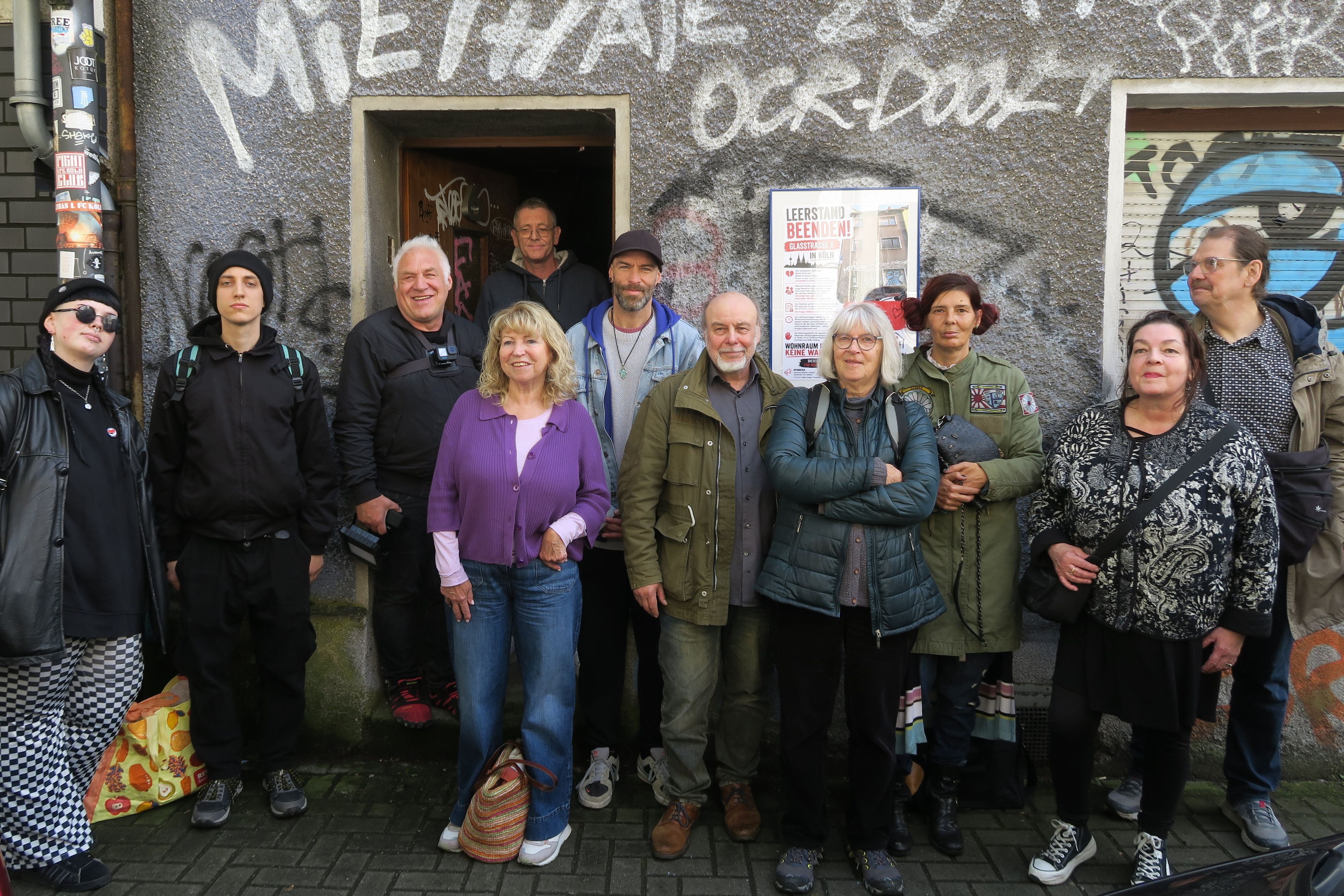 Eine Gruppe Menschen steht vor einem Haus mit beschmierter Fassade.