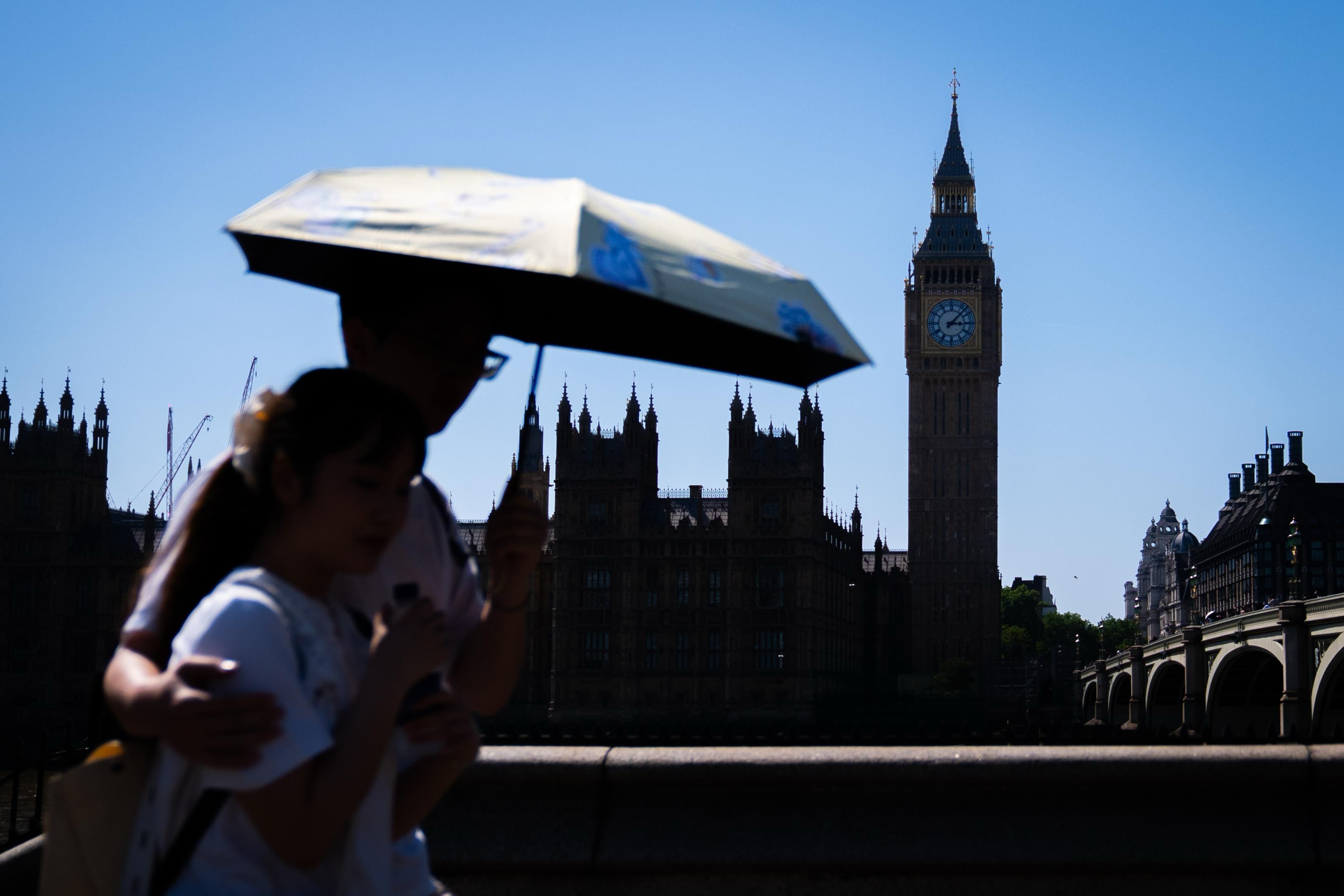 Touristen schützen sich vor dem heißen Wetter unter einem Regenschirm auf der Westminster Bridge im Zentrum Londons.