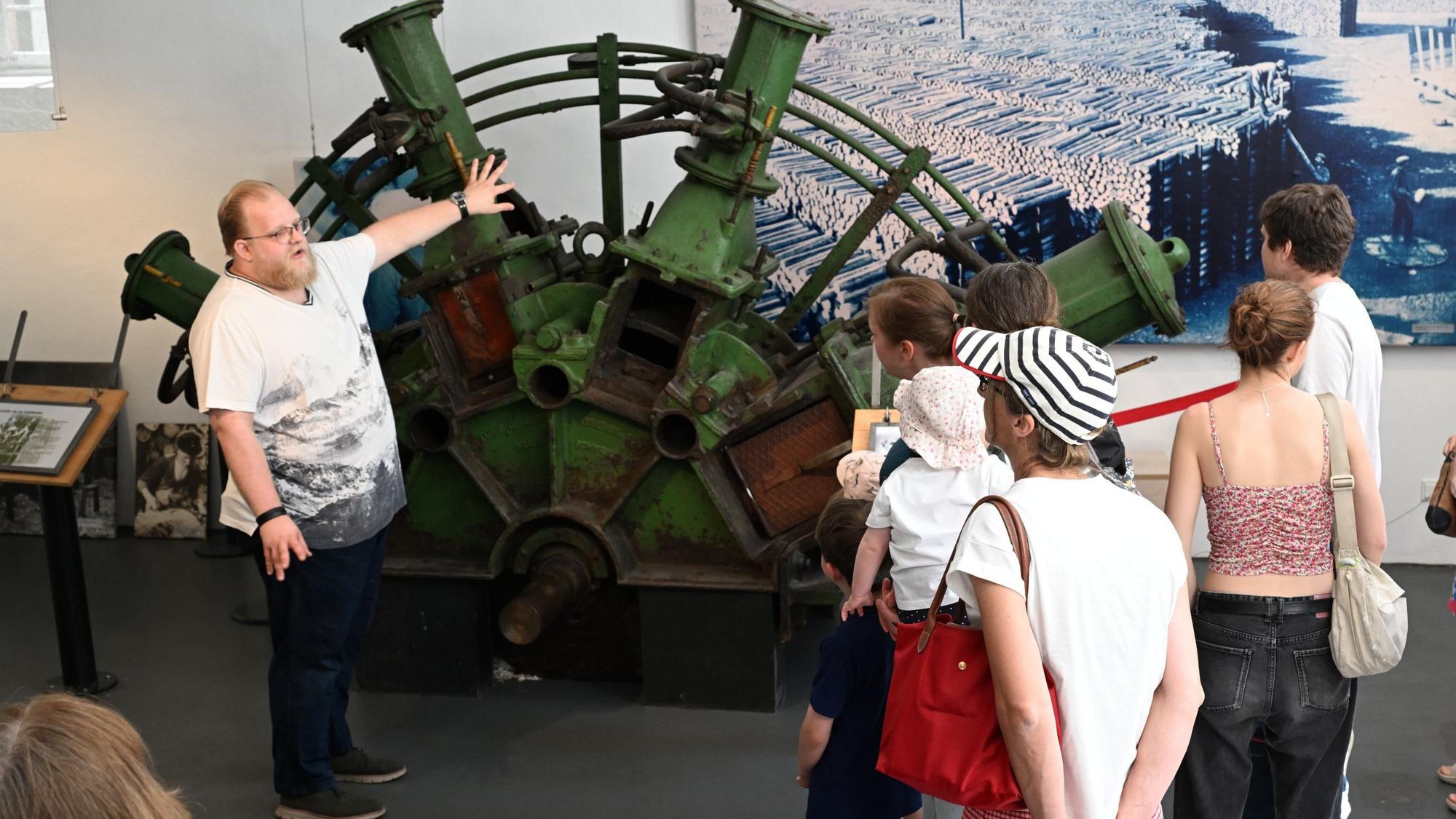 Zu sehen ist ein Museumsguide vor einer Gruppe, wie er über ein Ausstellungsstück spricht.