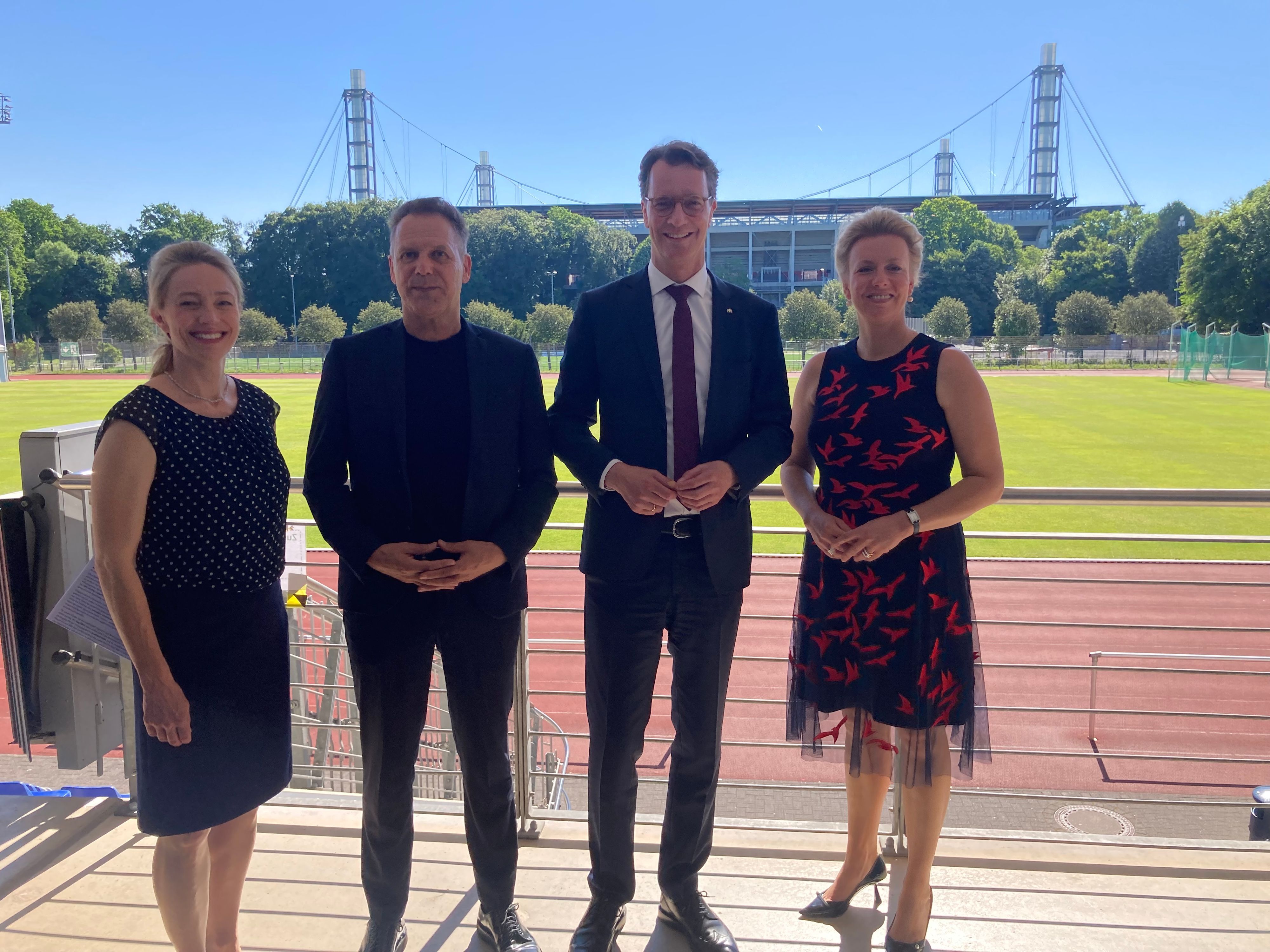Marion Steffen, Ansgar Thiel, Hendrik Wüst und Ina Brandes stehen vor einem Sportplatz der Sporthochschule.