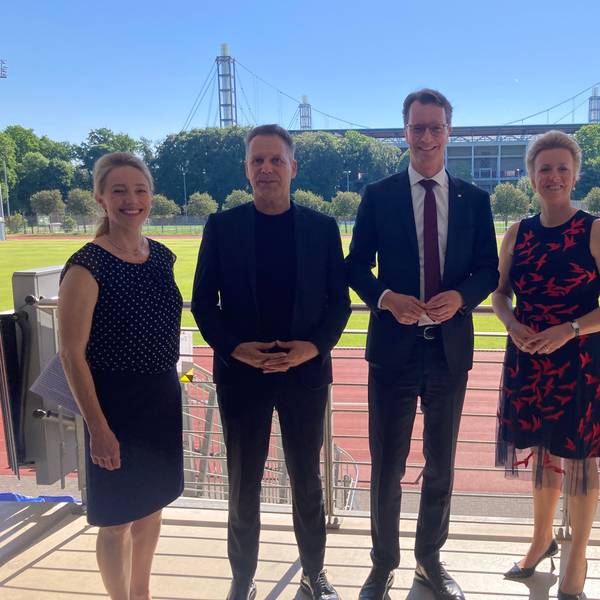 Marion Steffen, Ansgar Thiel, Hendrik Wüst und Ina Brandes stehen vor einem Sportplatz der Sporthochschule.