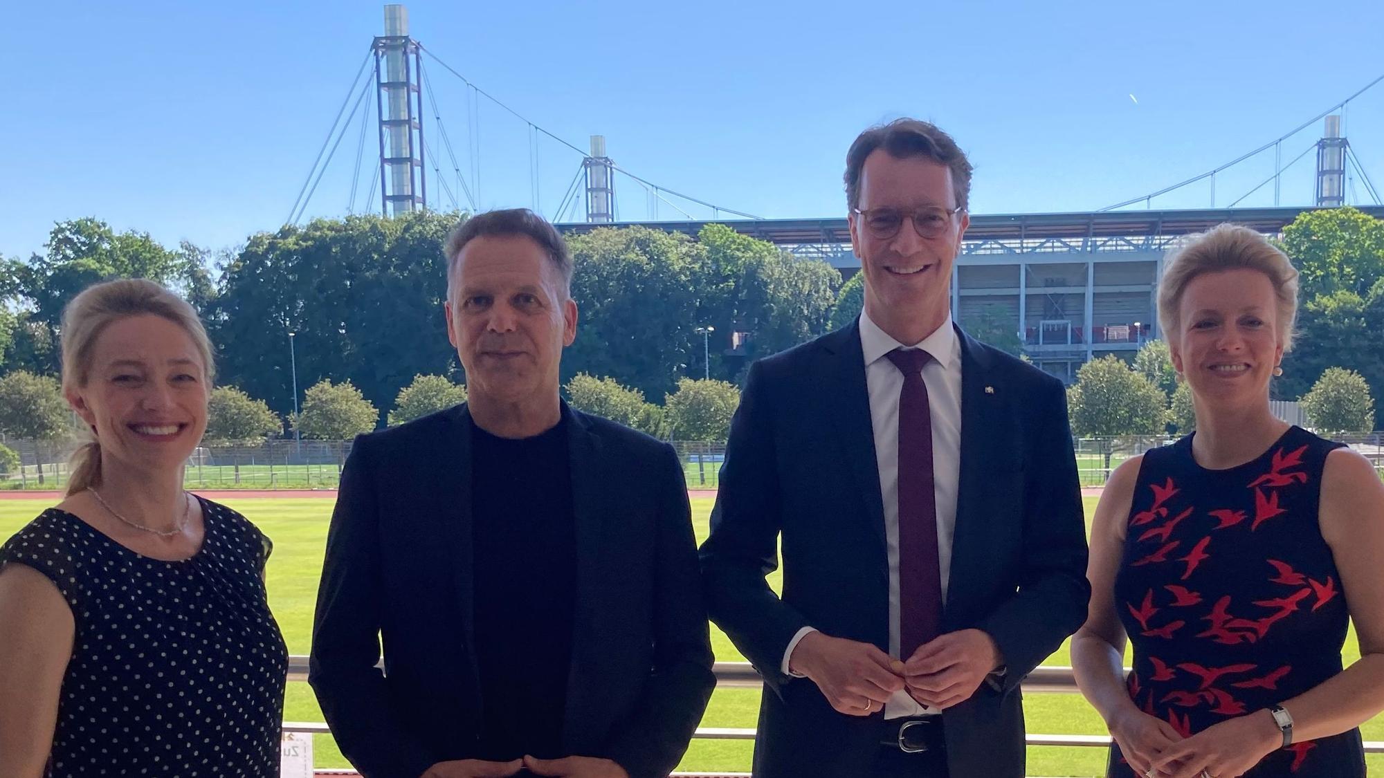 Marion Steffen, Ansgar Thiel, Hendrik Wüst und Ina Brandes stehen vor einem Sportplatz der Sporthochschule.