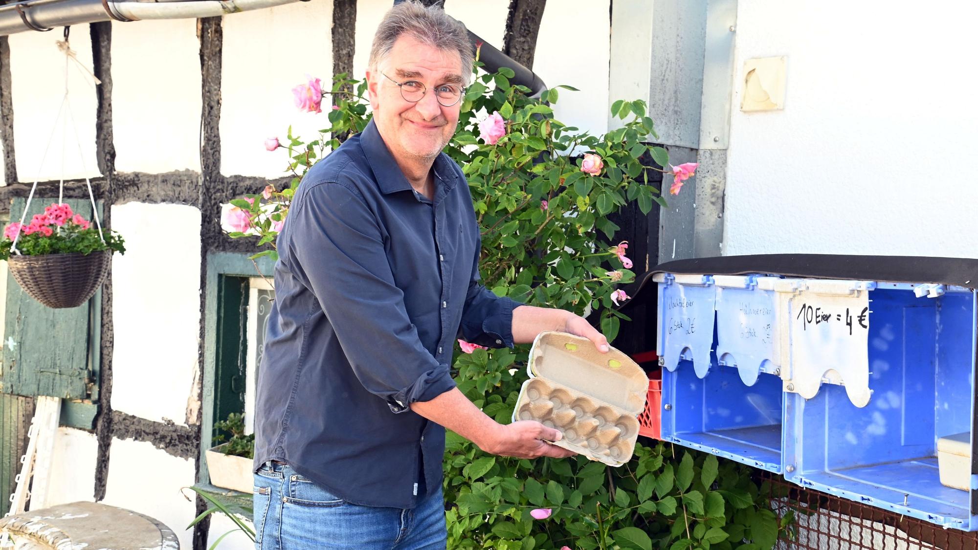 Ein Mann in blauem Hemd und Jeans hält einen leeren Eierkarton.