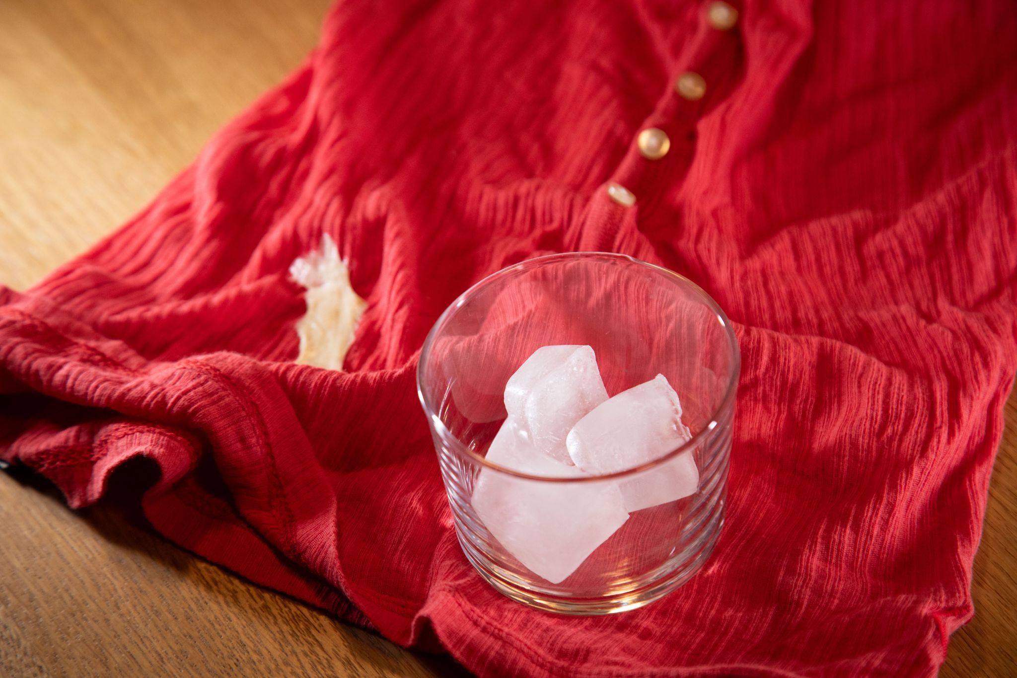 Glas mit Eiswürfeln steht auf einem Shirt mit Kaugummi-Fleck