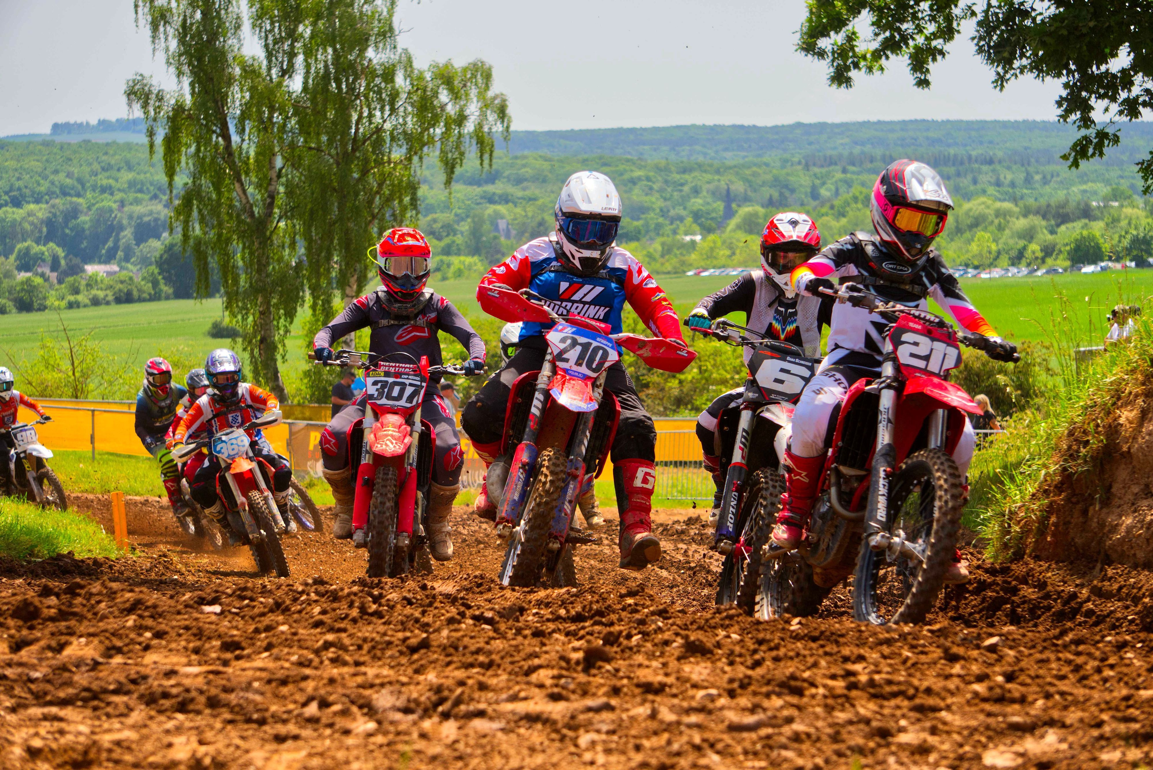 Motocross-Fahrer hinter- und nebeneinander fahren über eine schlammige Strecke.