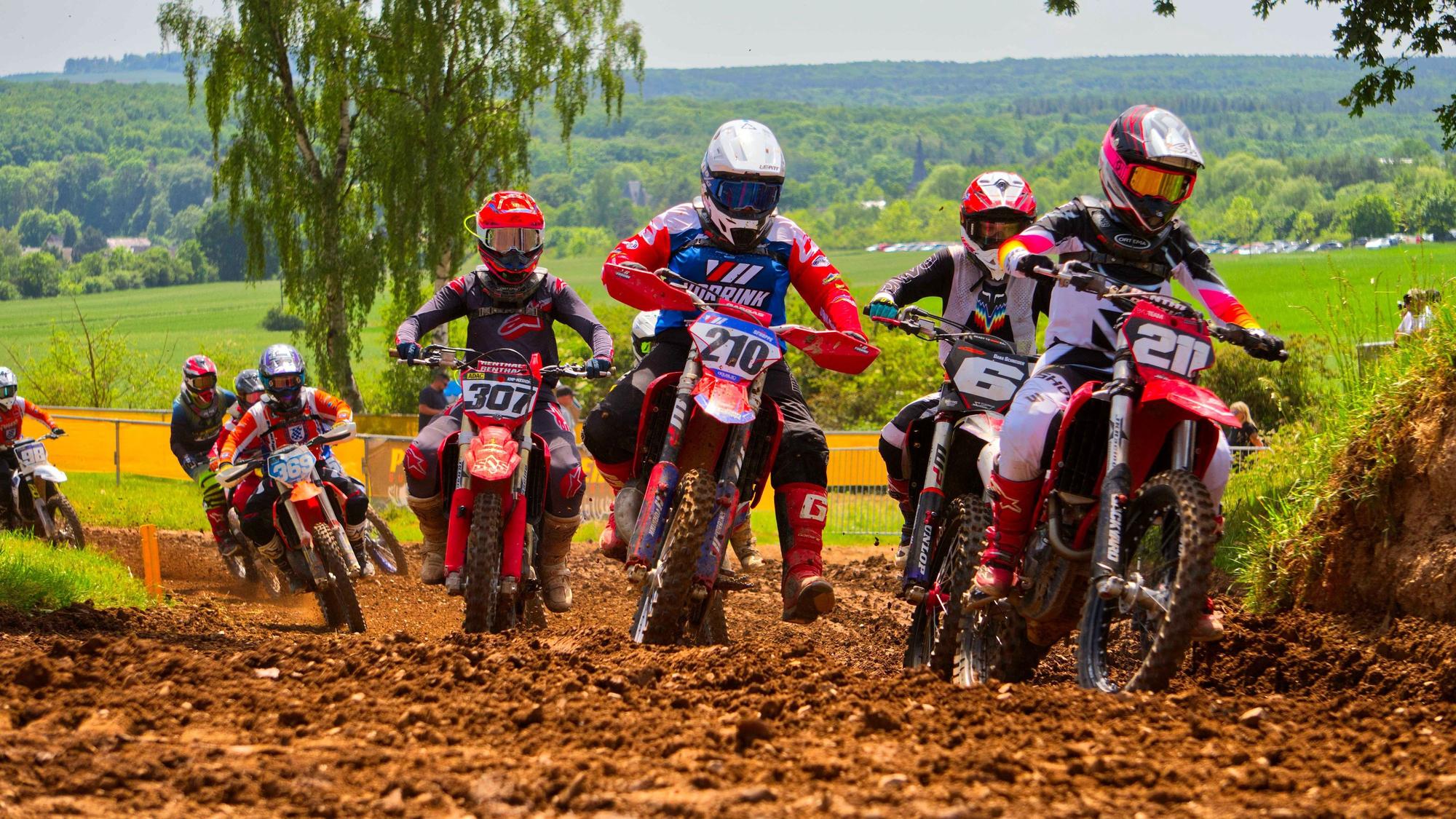 Motocross-Fahrer hinter- und nebeneinander fahren über eine schlammige Strecke.