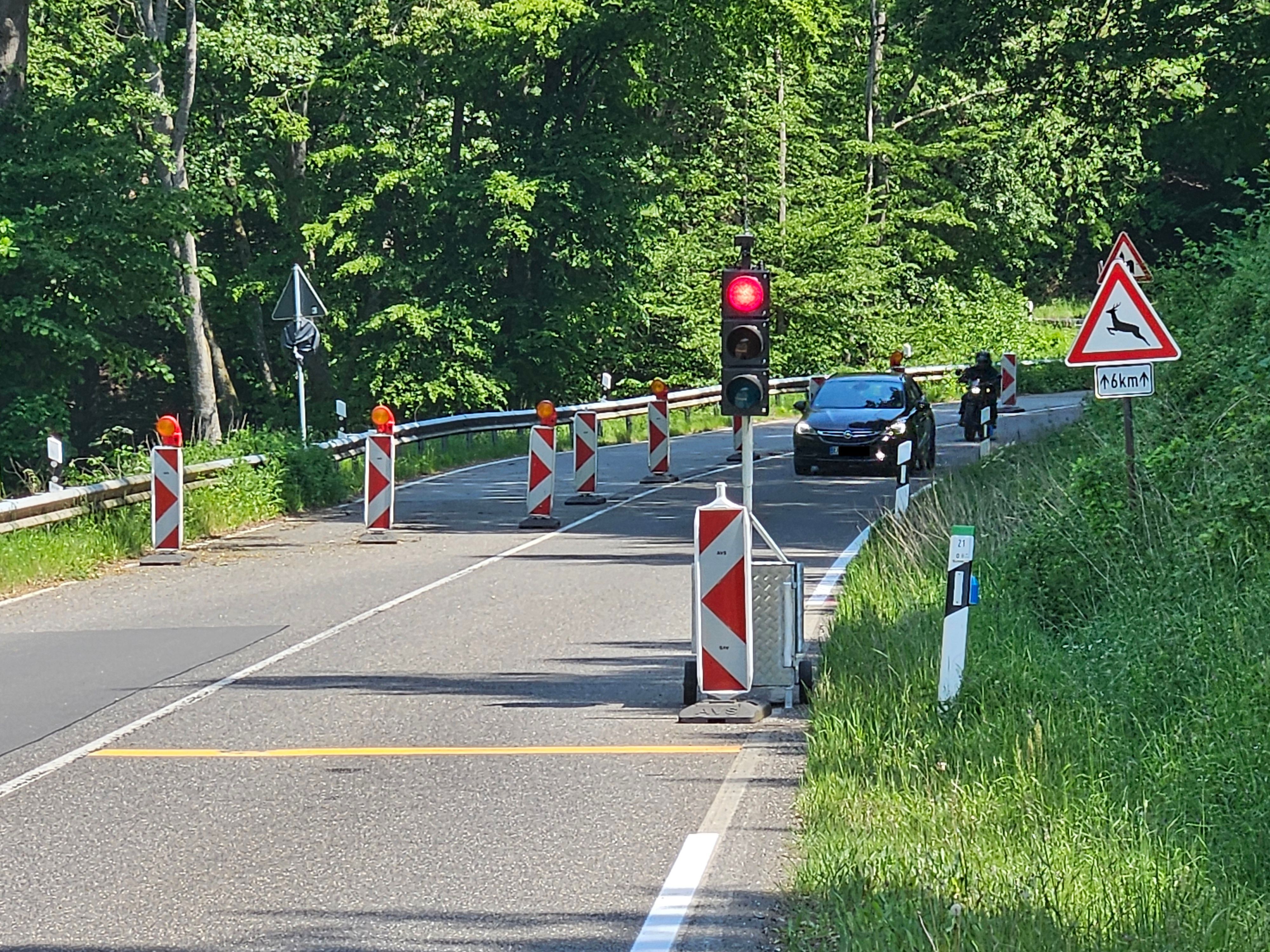 Blick auf die halbseitig abgesperrte Straße und eine rote Ampel im Vordergrund. Ein Auto und ein Motorrad kommen entgegen.