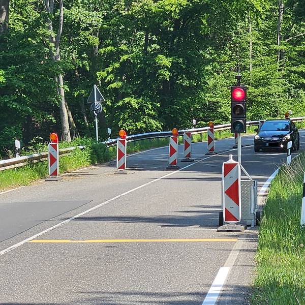 Blick auf die halbseitig abgesperrte Straße und eine rote Ampel im Vordergrund. Ein Auto und ein Motorrad kommen entgegen.
