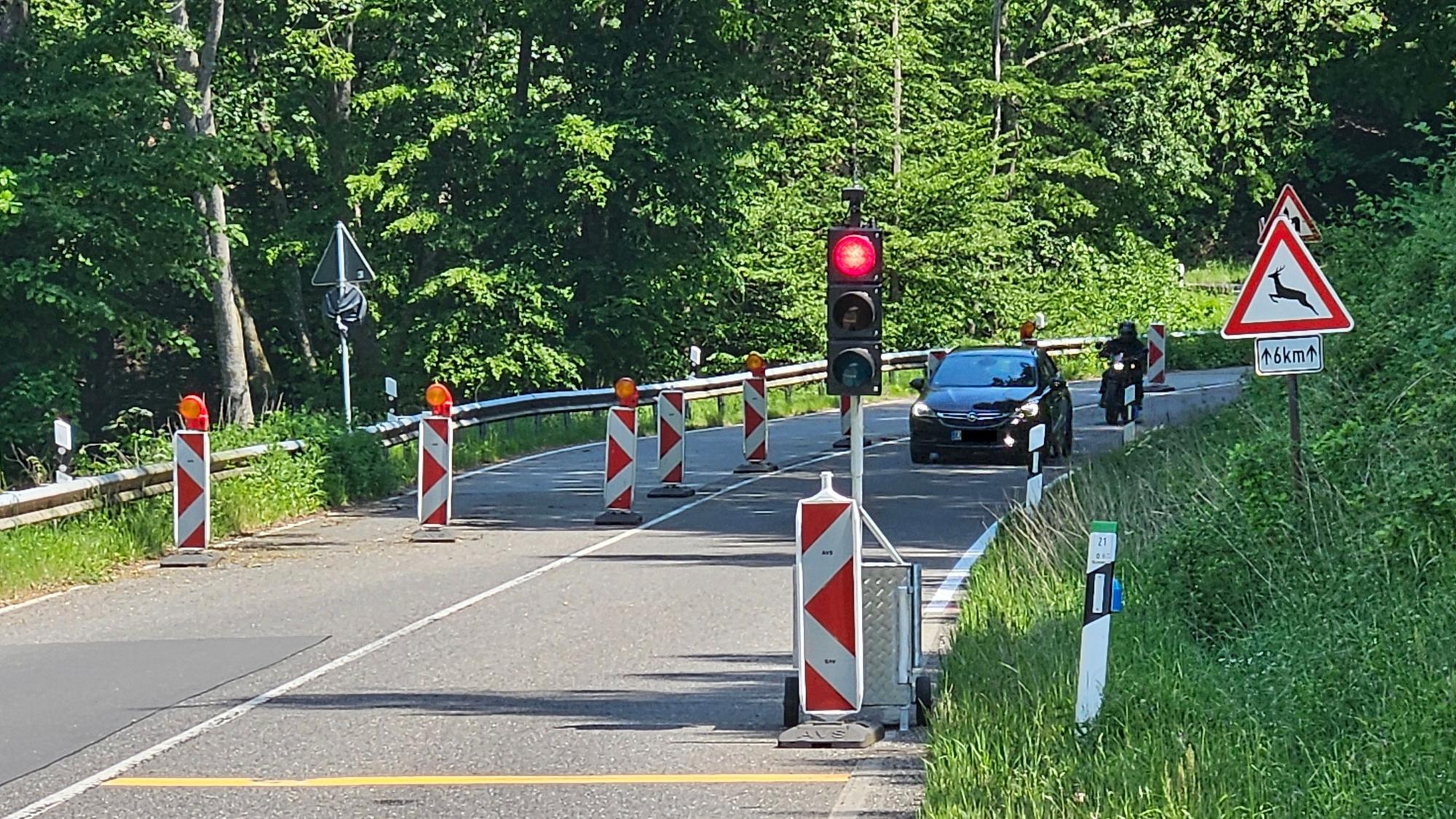 Blick auf die halbseitig abgesperrte Straße und eine rote Ampel im Vordergrund. Ein Auto und ein Motorrad kommen entgegen.