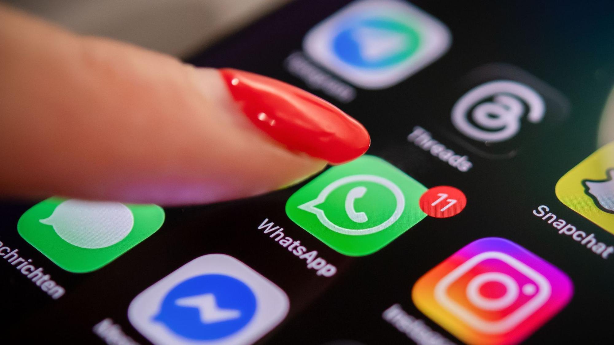 Eine Frau tippt auf einem Smartphone auf das WhatsApp-Symbol