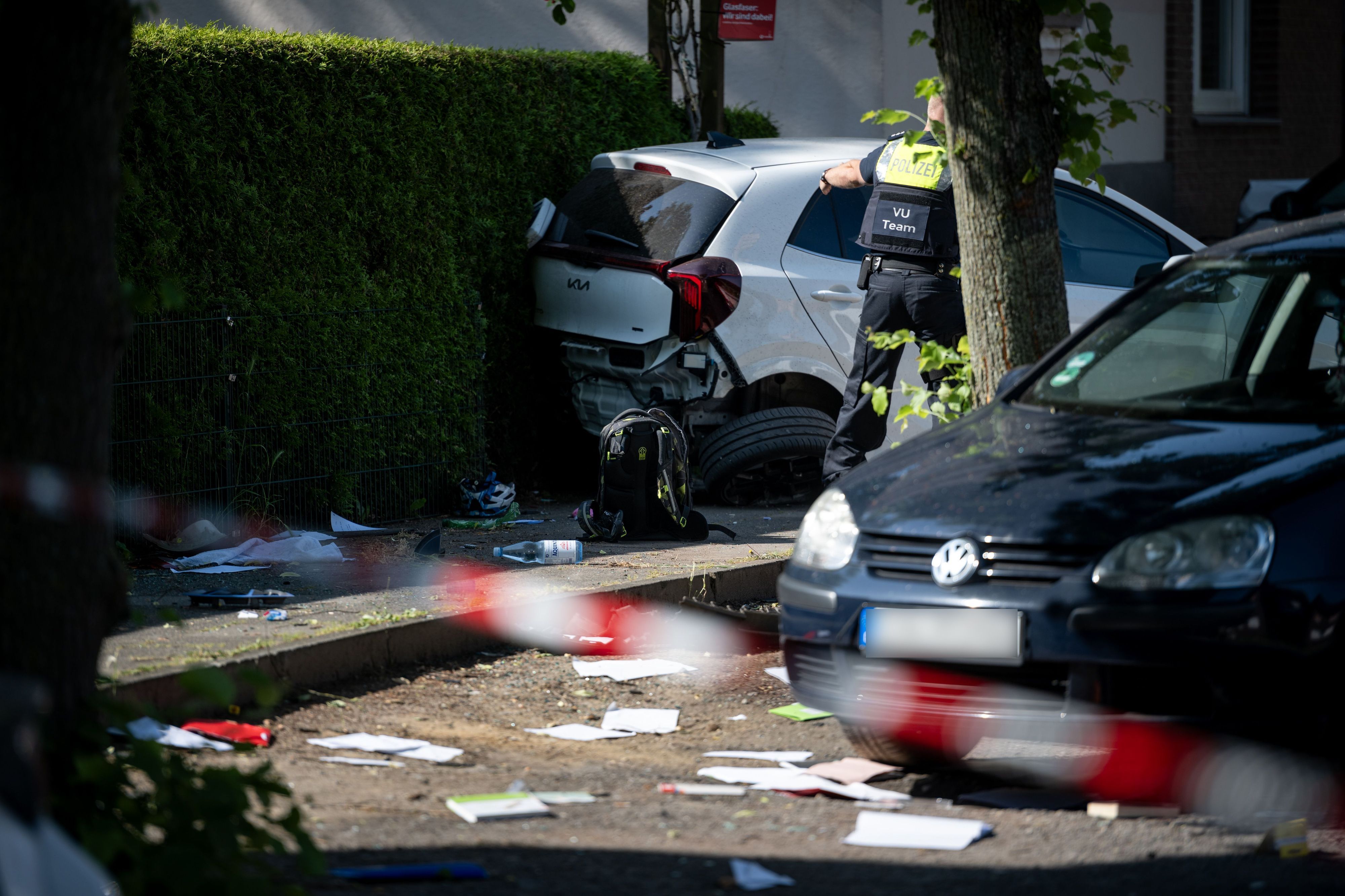 Ein Schulrucksack liegt auf dem Boden vor beschädigten Autos. Die Polizei sichert eine Unfallstelle, nachdem eine Autofahrerin drei Kinder vor einer Schule in Dinslaken verletzt hat.