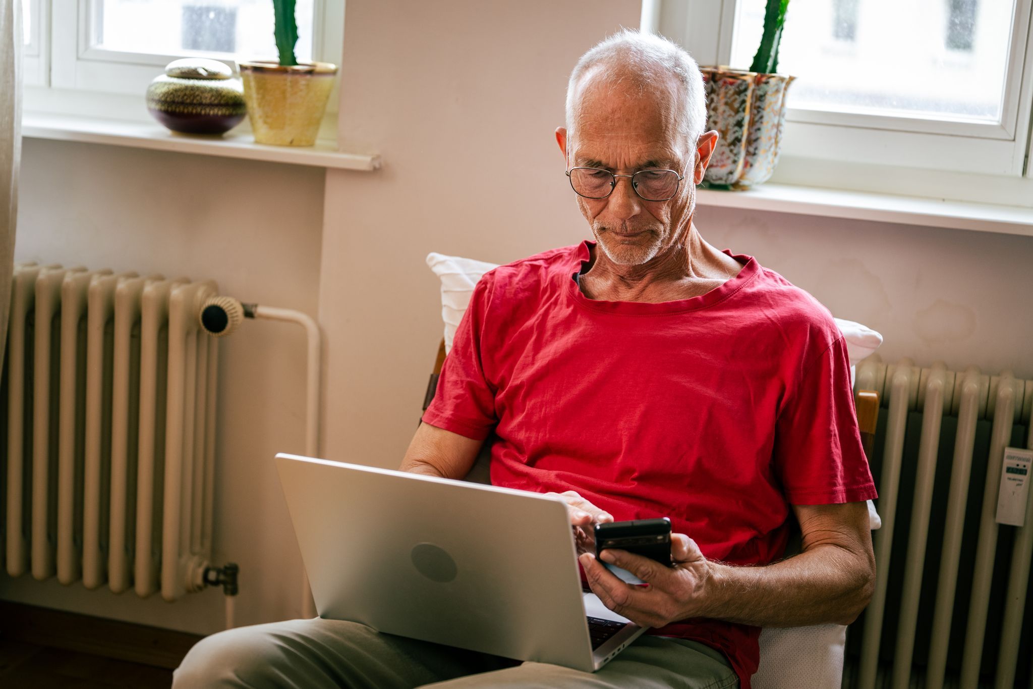 Ein Senior sitzt mit Laptop und Smartphone auf einem Sessel