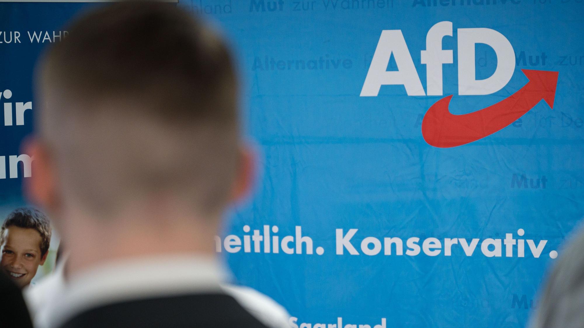Ein Anhänger der AfD im Saarland steht auf einer Wahlparty vor einem Aufsteller der Partei.