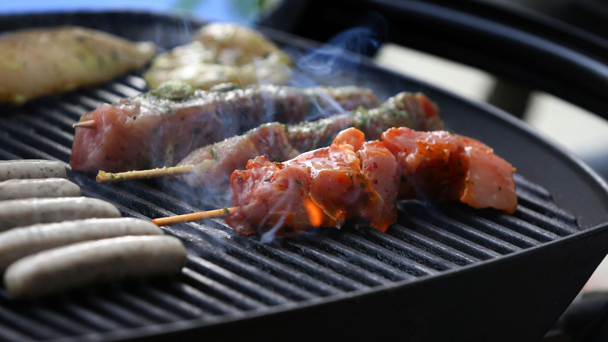 Fleischspieße, Bratwürste und Steaks liegen auf dem Rost eines Gasgrills.