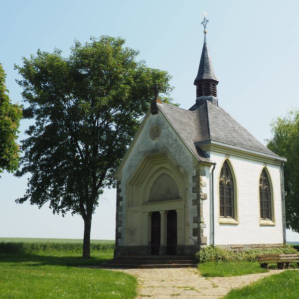 Die Kapelle steht zwischen Bäumen, ein Kiesweg führt zum Eingang.