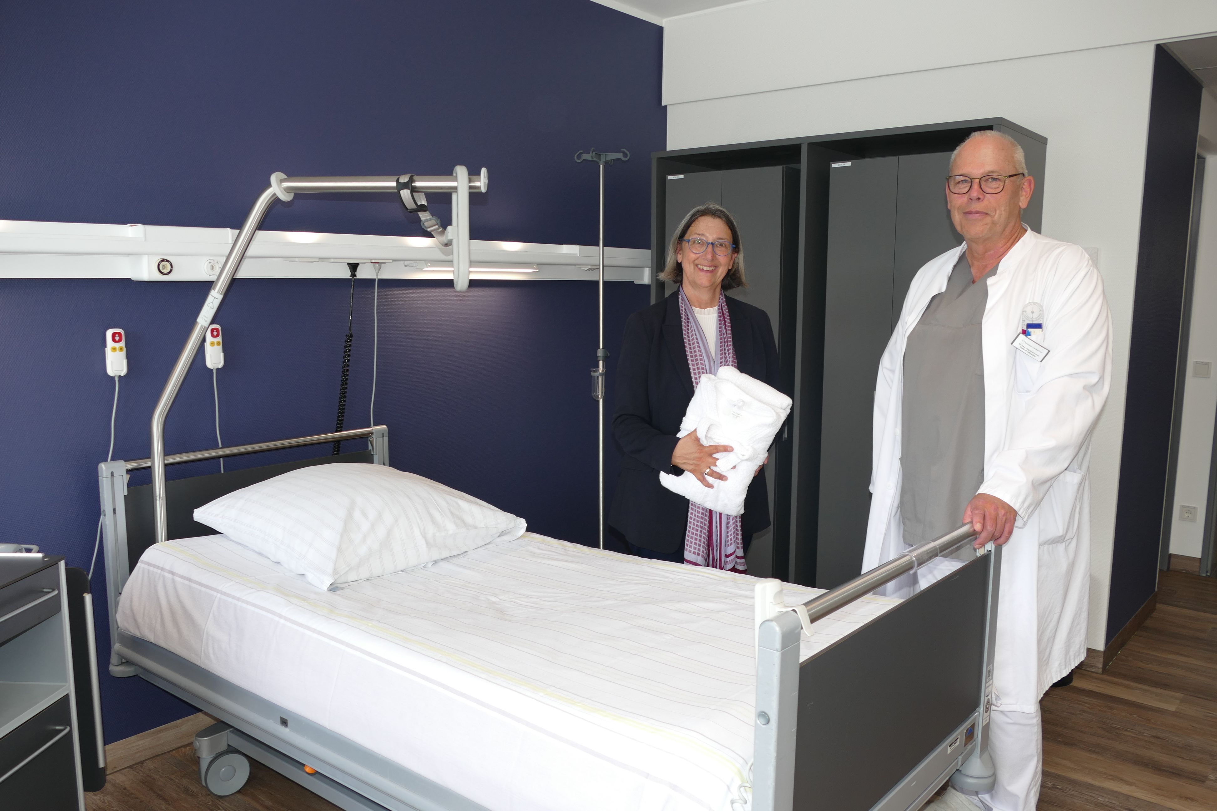 Ein Arzt und eine Frau in Zivilkleidung an einem Krankenbett.