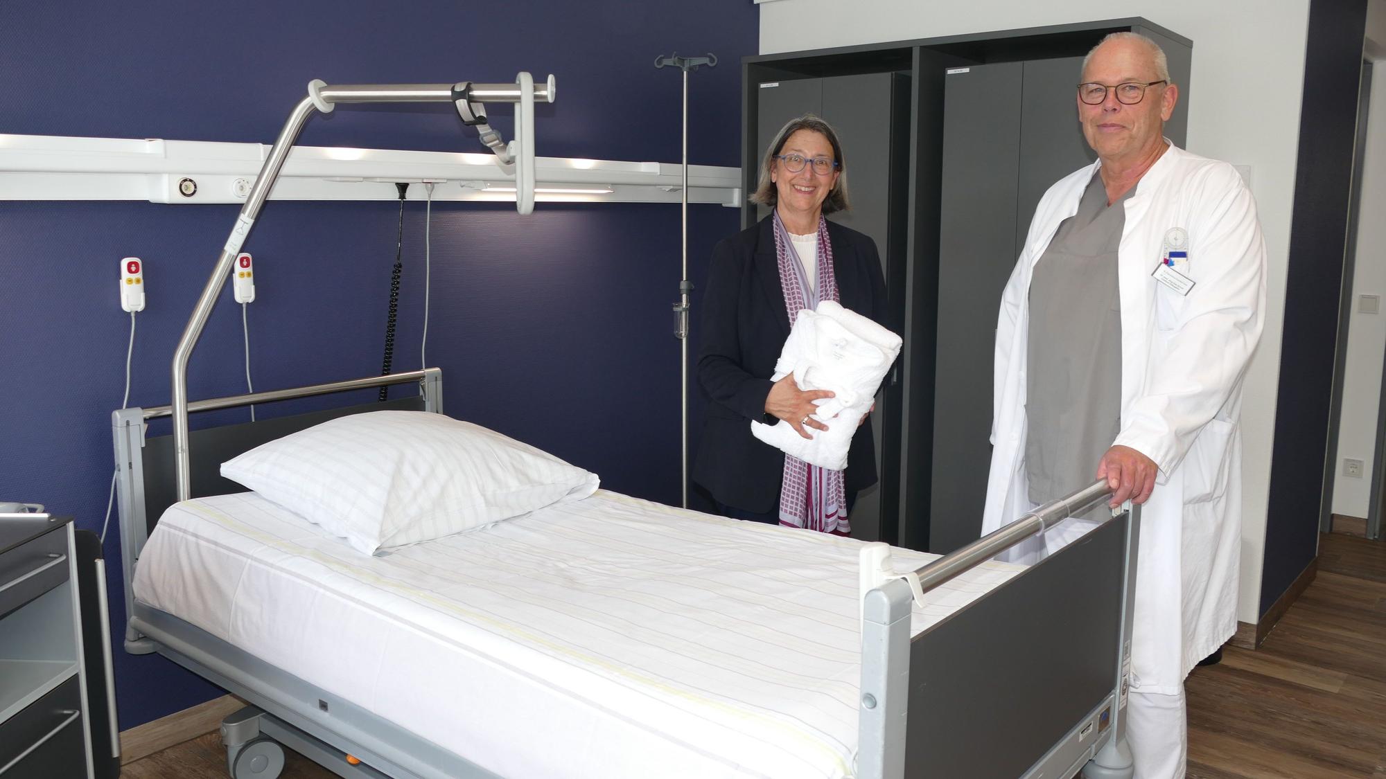 Ein Arzt und eine Frau in Zivilkleidung an einem Krankenbett.